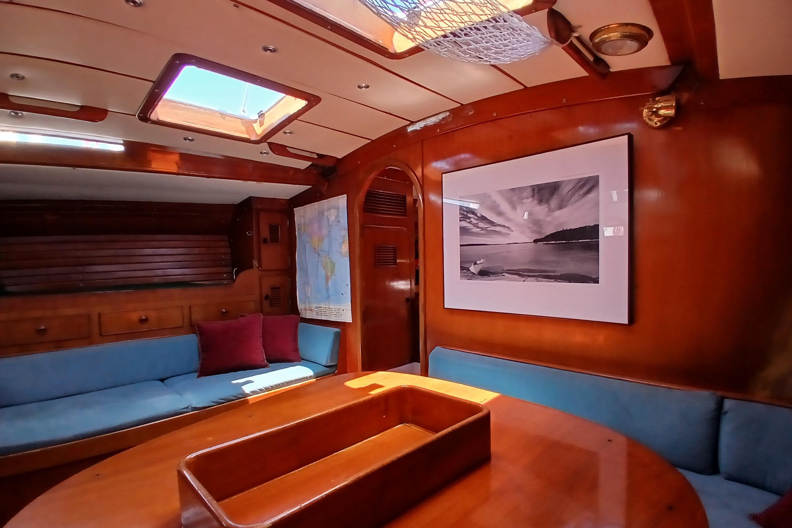 Cozy 1981 SKYE 51 yacht interior with wooden decor, blue seating, and nautical artwork.