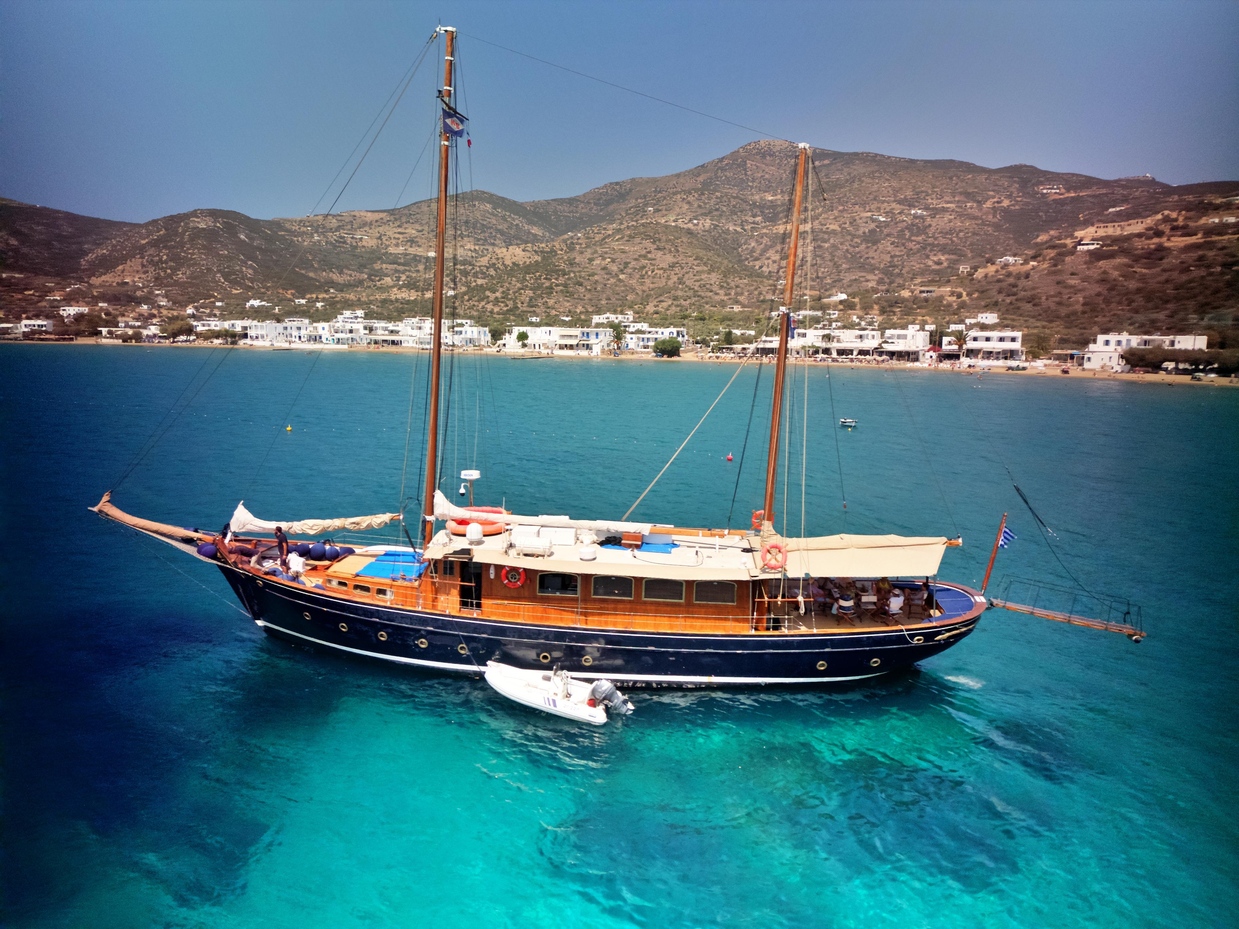 Vintage 1969 Psarros Shipyard yacht sailing in clear blue waters near coastal town.