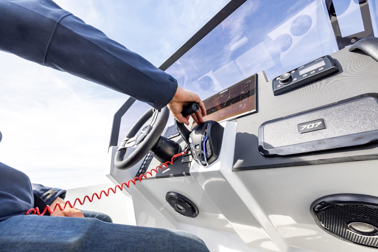Person operating Iron 707 boat controls, 2022 model, with steering wheel and dashboard.