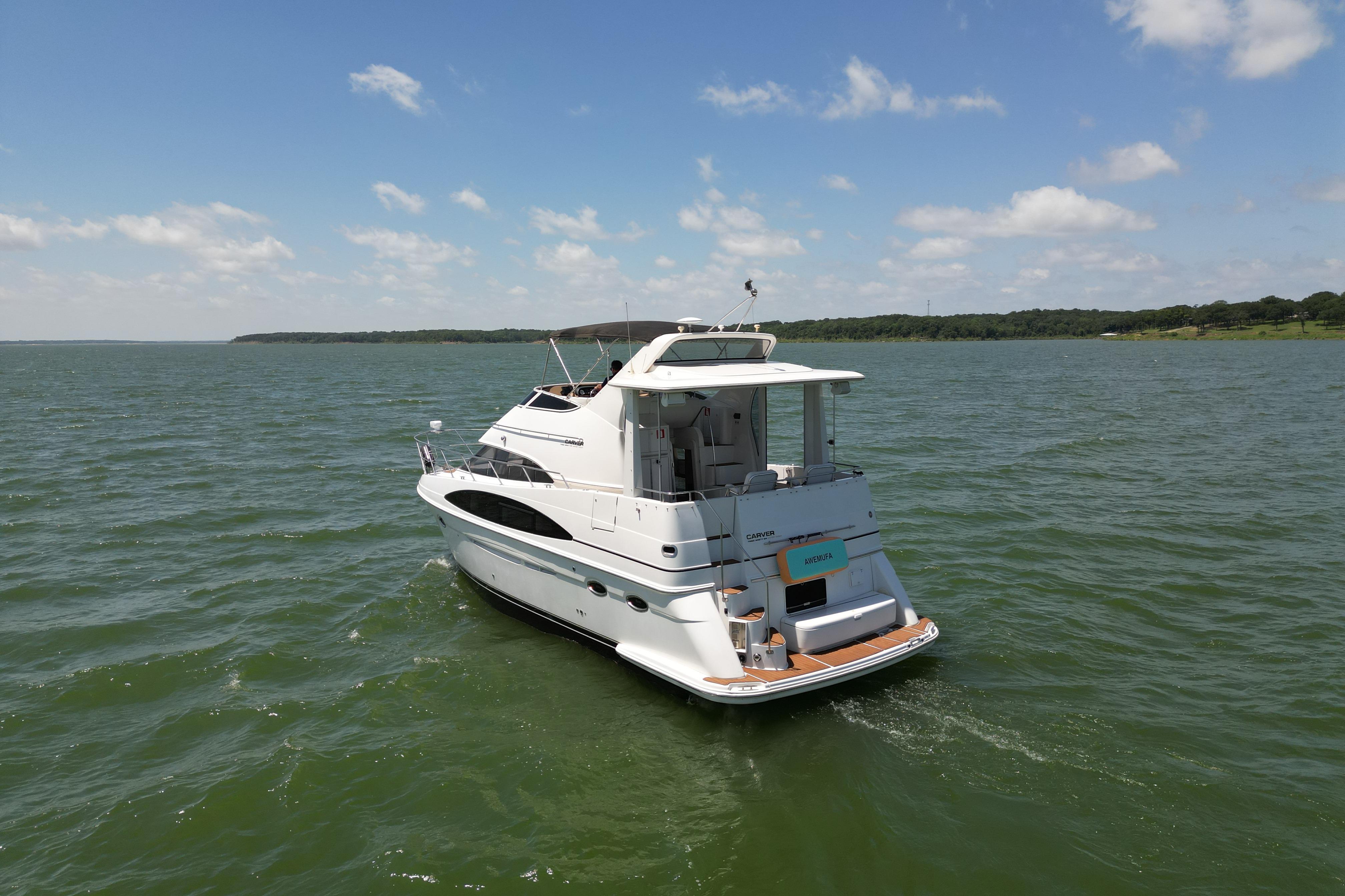 2002 Carver 396 Motor Yacht cruising on a serene lake under a clear blue sky.