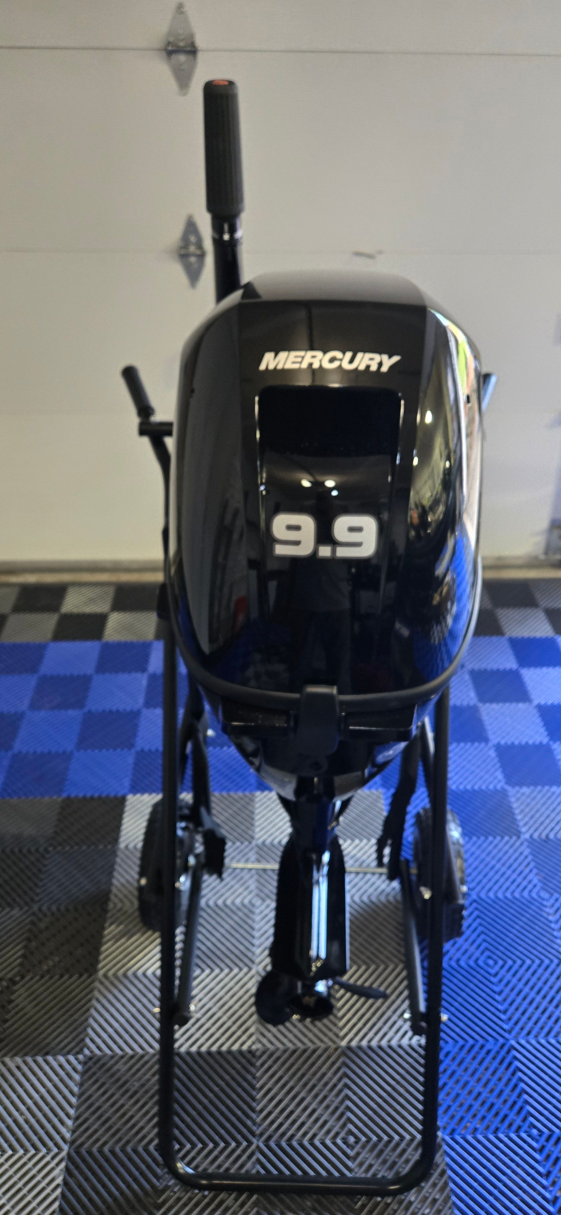 A Mercury 9.9 outboard motor stands on a blue and black checkered floor.