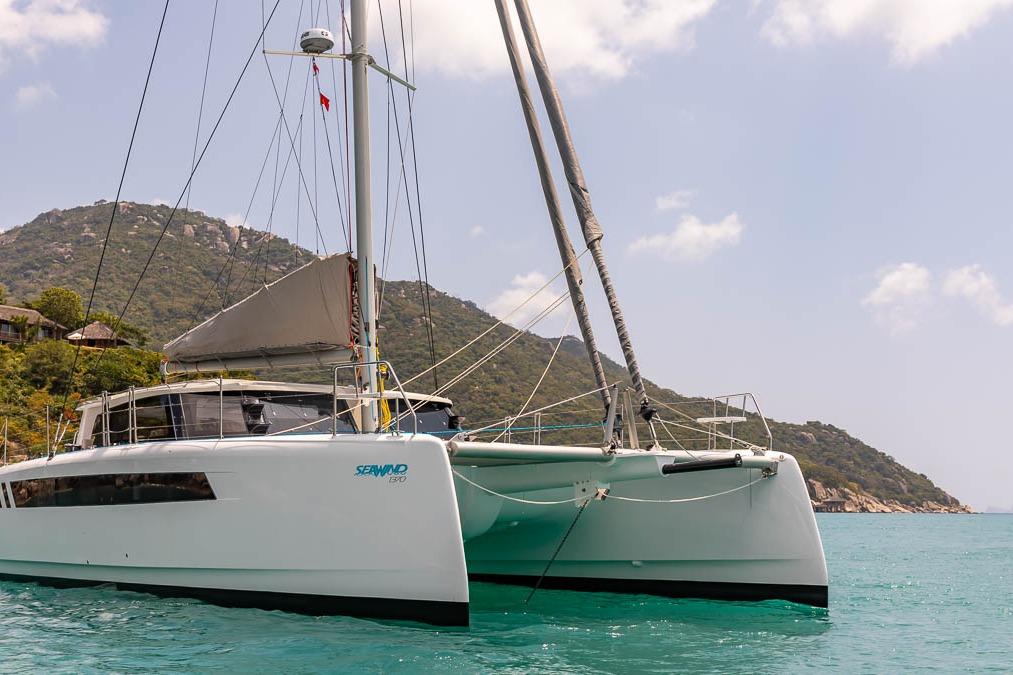 2026 Seawind 1370 catamaran sailing near scenic coastline with lush hills and clear blue water.