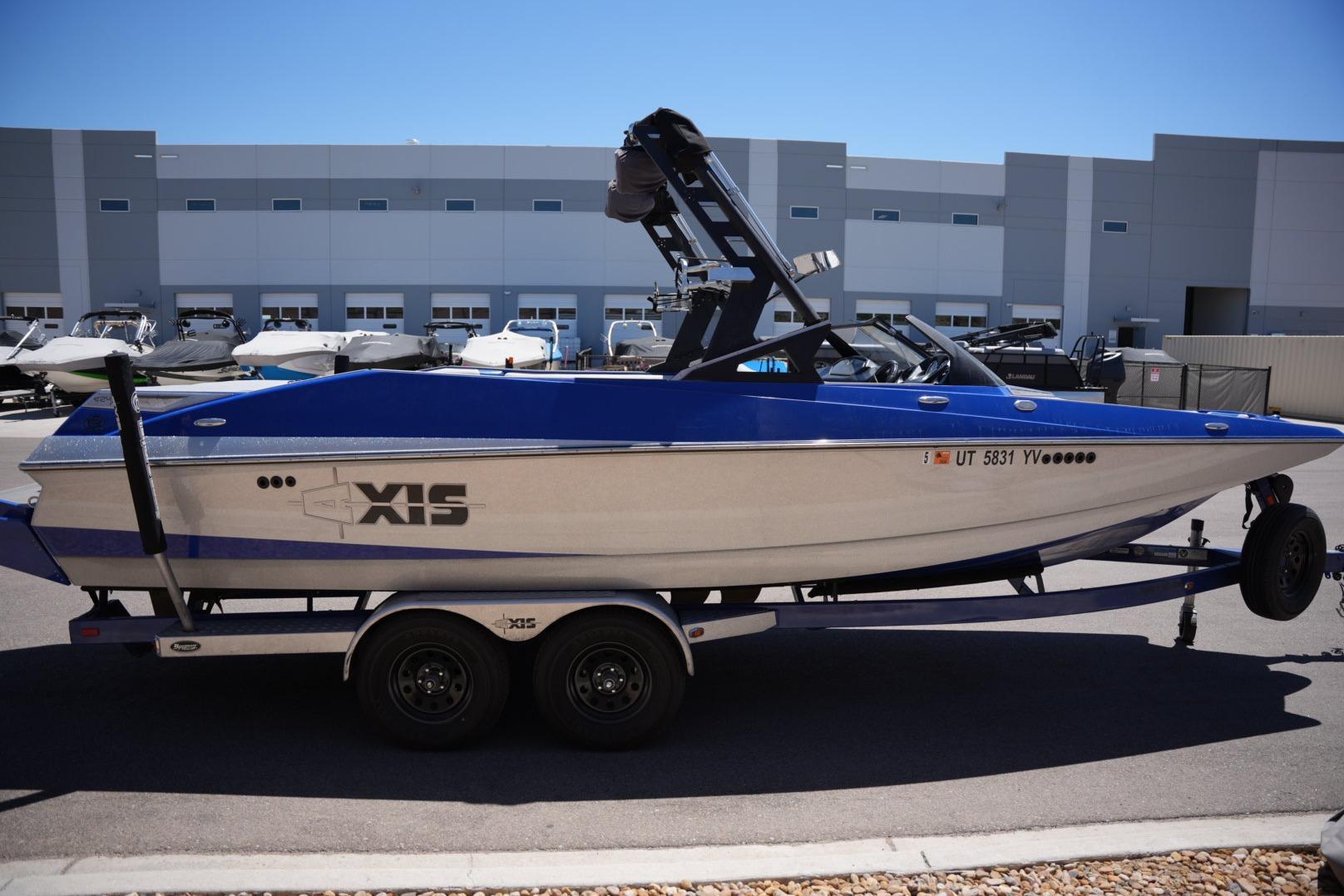 2015 Axis A24 boat on trailer, blue and white, parked outside a warehouse.
