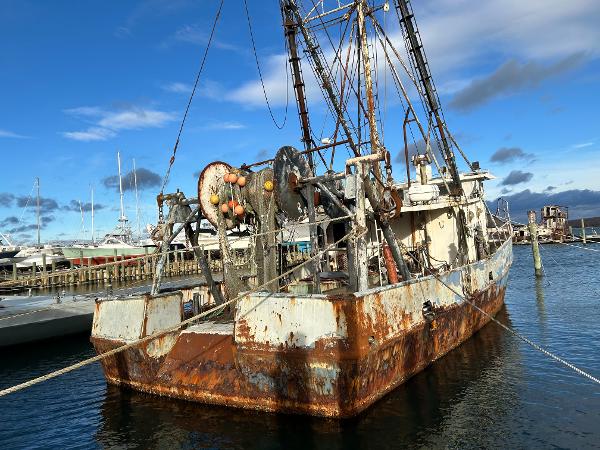 Old 1979 Custom Steel Trawler Dragger docked, showing rust and wear against a clear blue sky.
