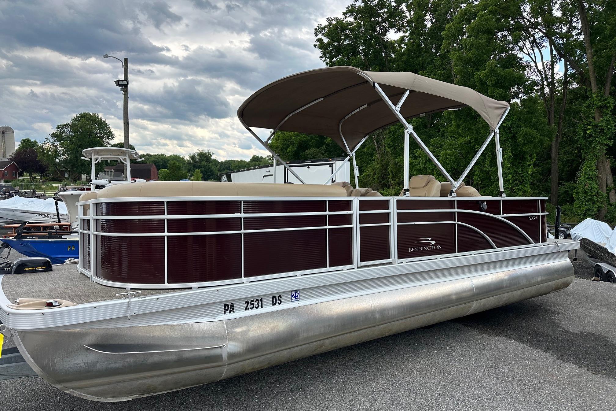 2016 Bennington 24 SCWX pontoon boat with canopy, parked on a trailer, surrounded by trees.