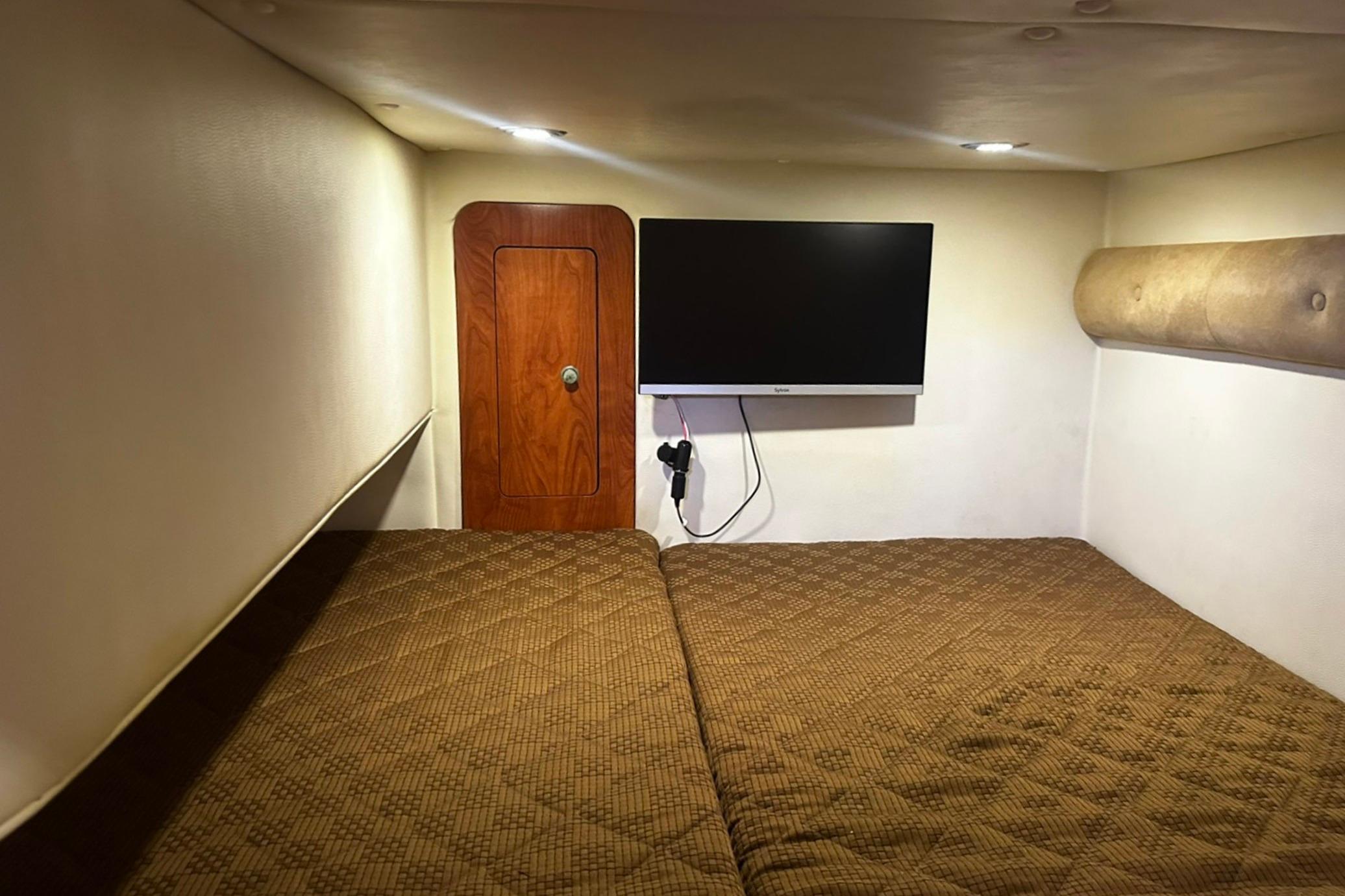Interior cabin of 2012 Rinker 310 Express Cruiser LE with TV and cozy bedding.