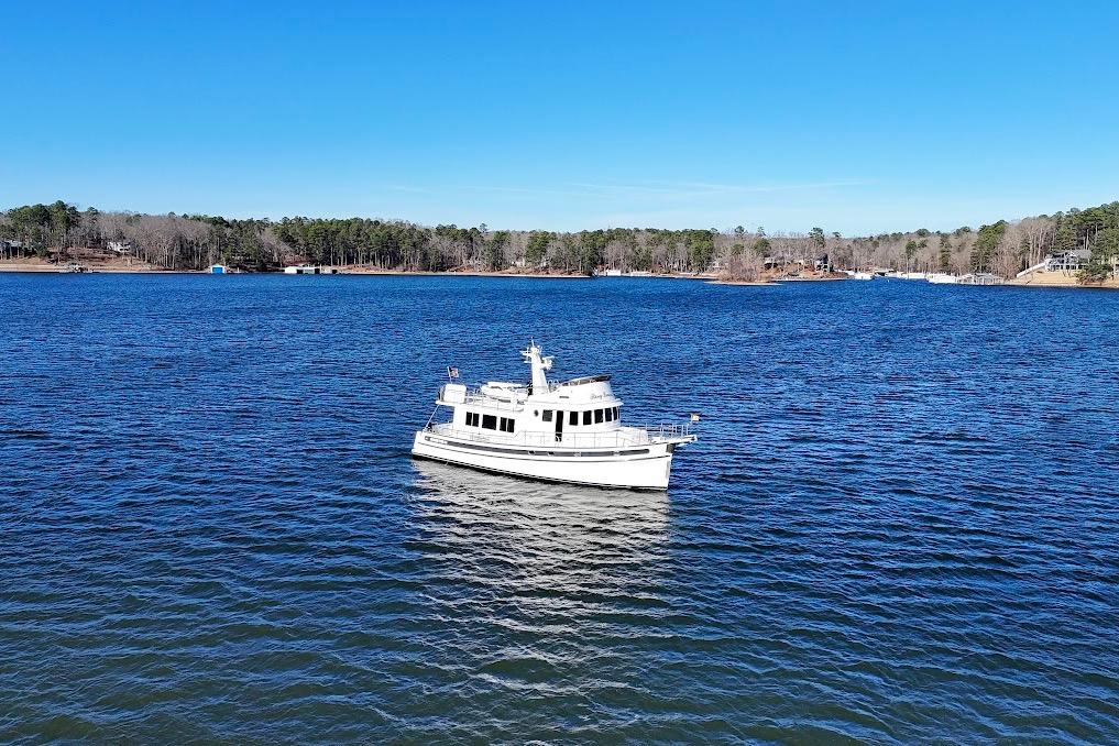 2007 Nordic Tug 54 cruising on a serene lake under a clear blue sky.