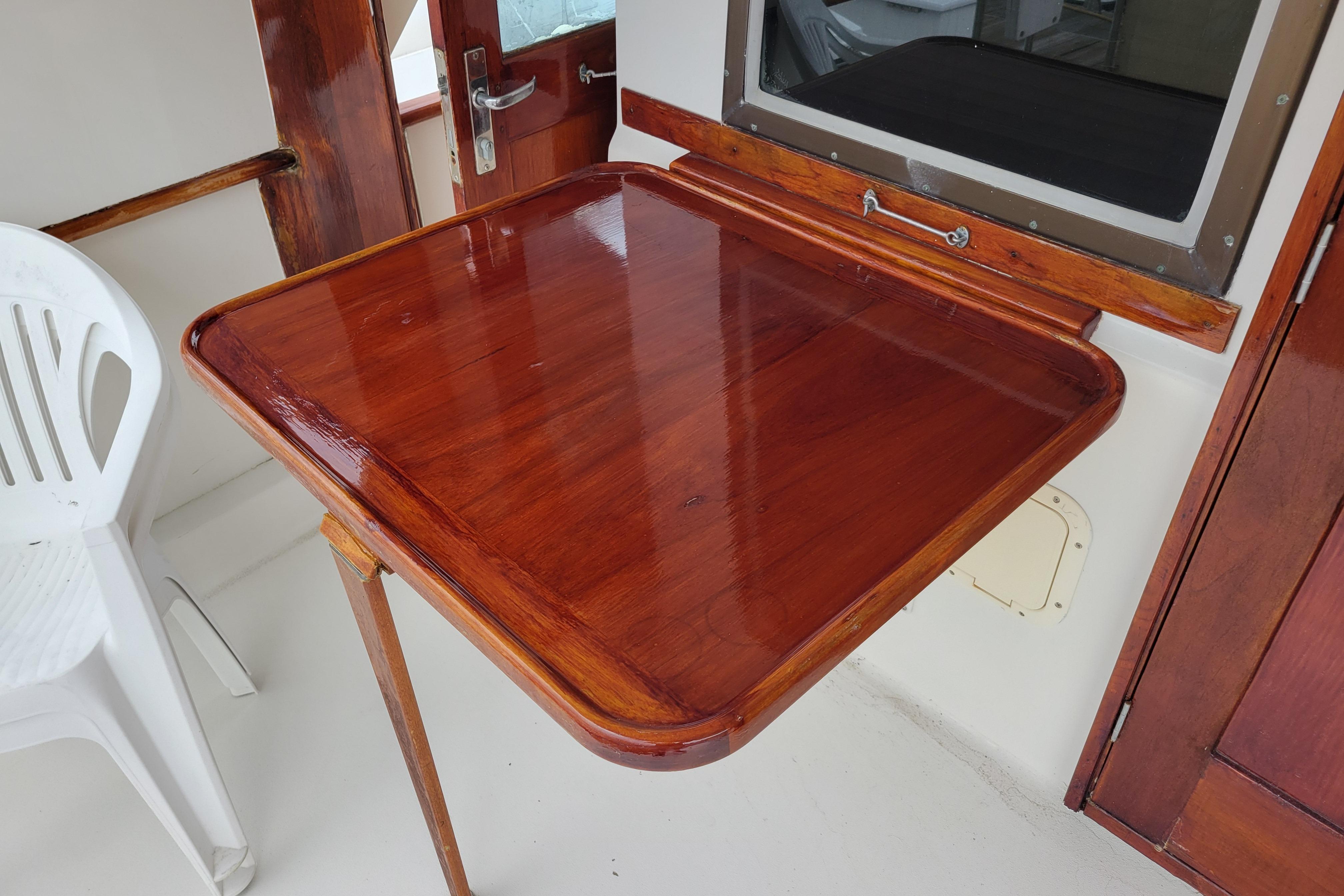 Polished wooden table on 1980 Hatteras 53 Yacht Fisherman, adjacent to white chair.