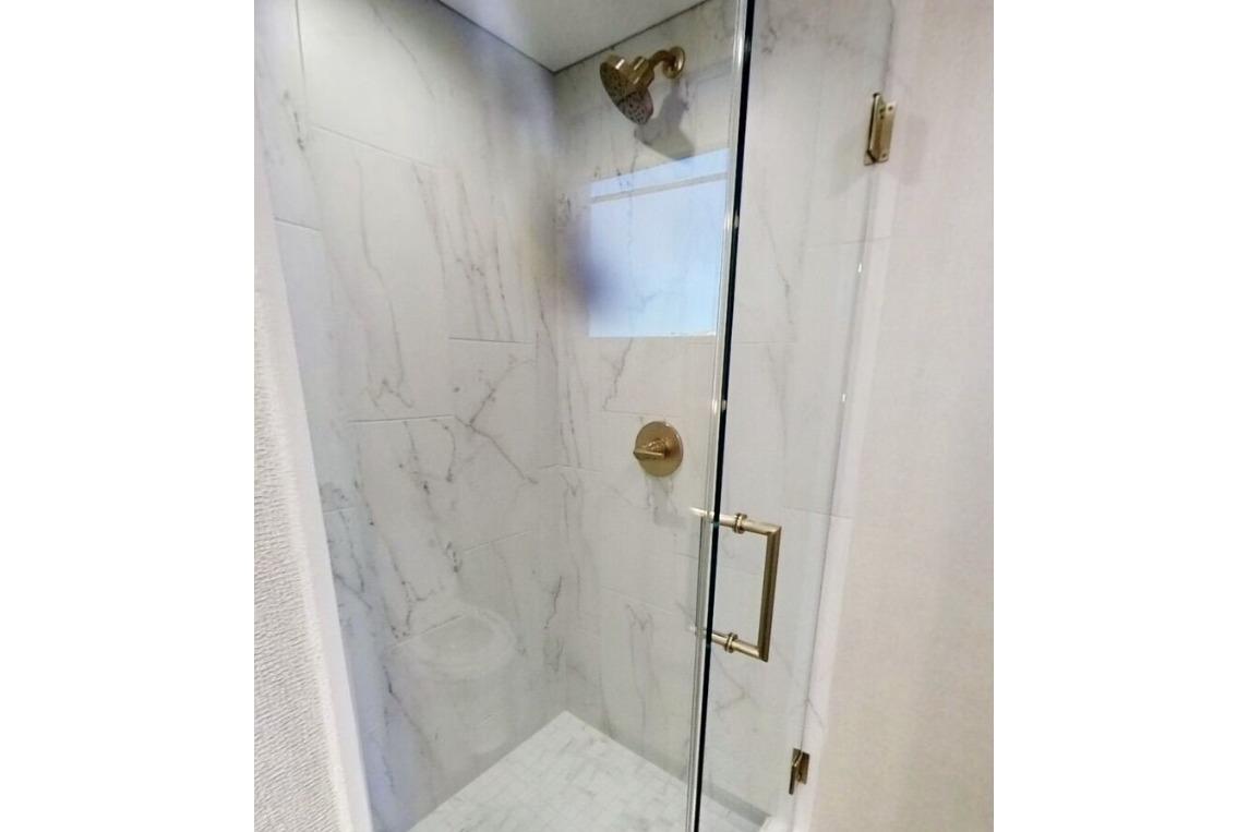 Luxurious marble shower with glass door and gold fixtures on Adonia's Galileo Trip #1, 2023.