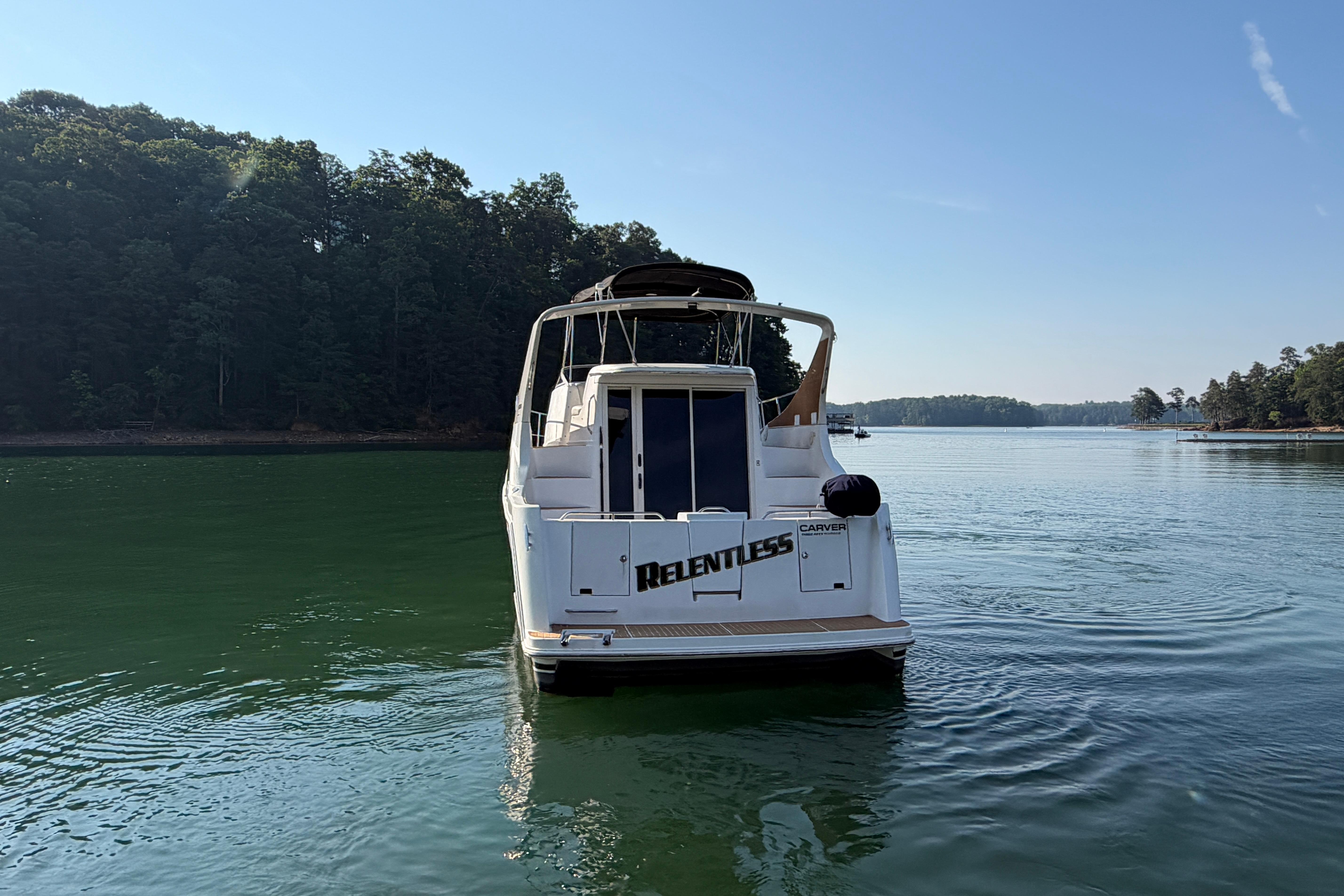 2003 Carver 350 Mariner yacht on serene lake, surrounded by lush trees.