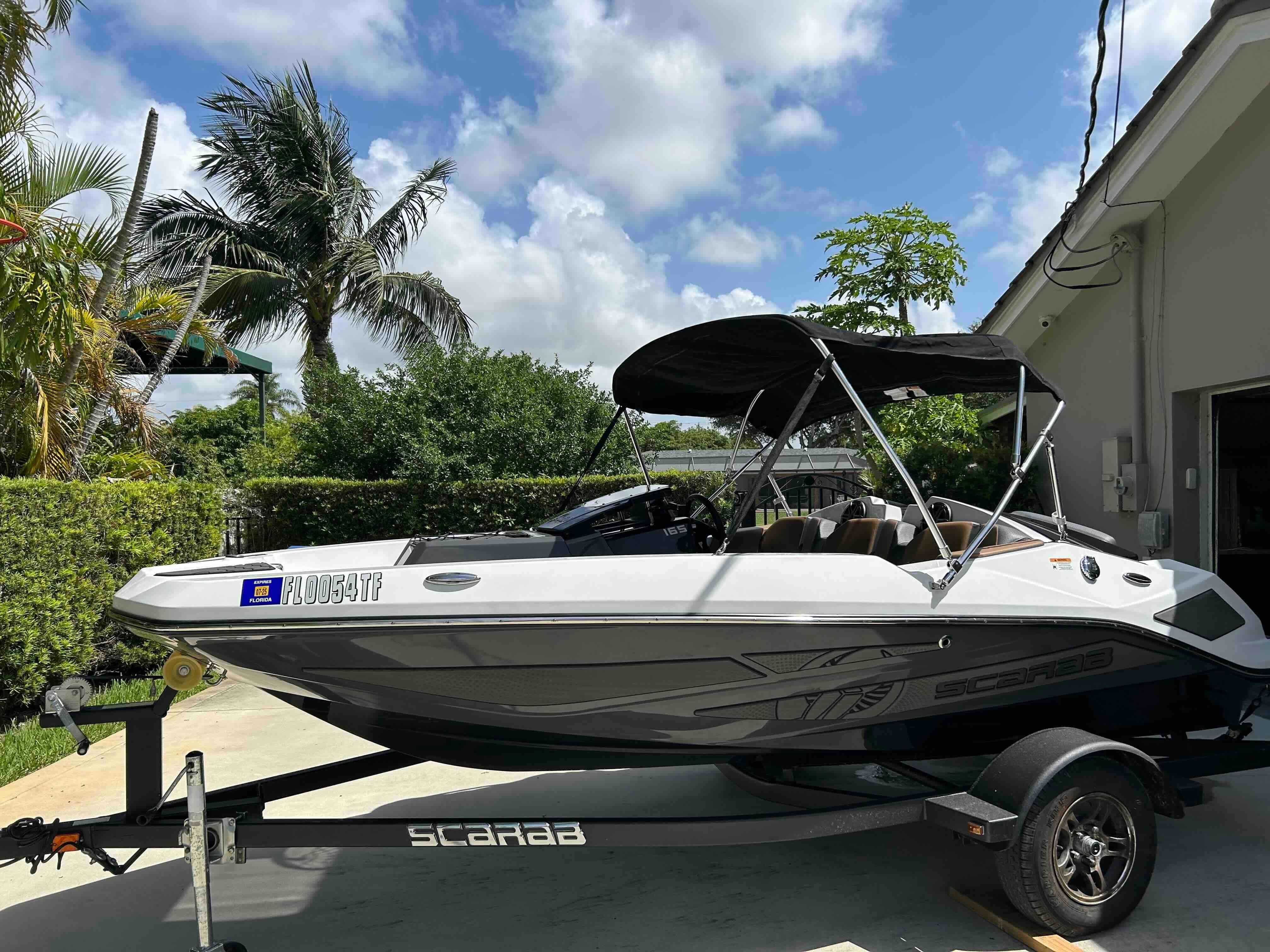 A 2022 Scarab 165 ID boat on a trailer in a sunny garden setting.