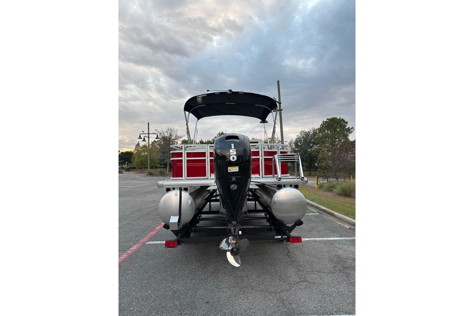 2026 Sun Tracker Fishin' Barge 22 DLX pontoon boat with outboard motor in parking lot.