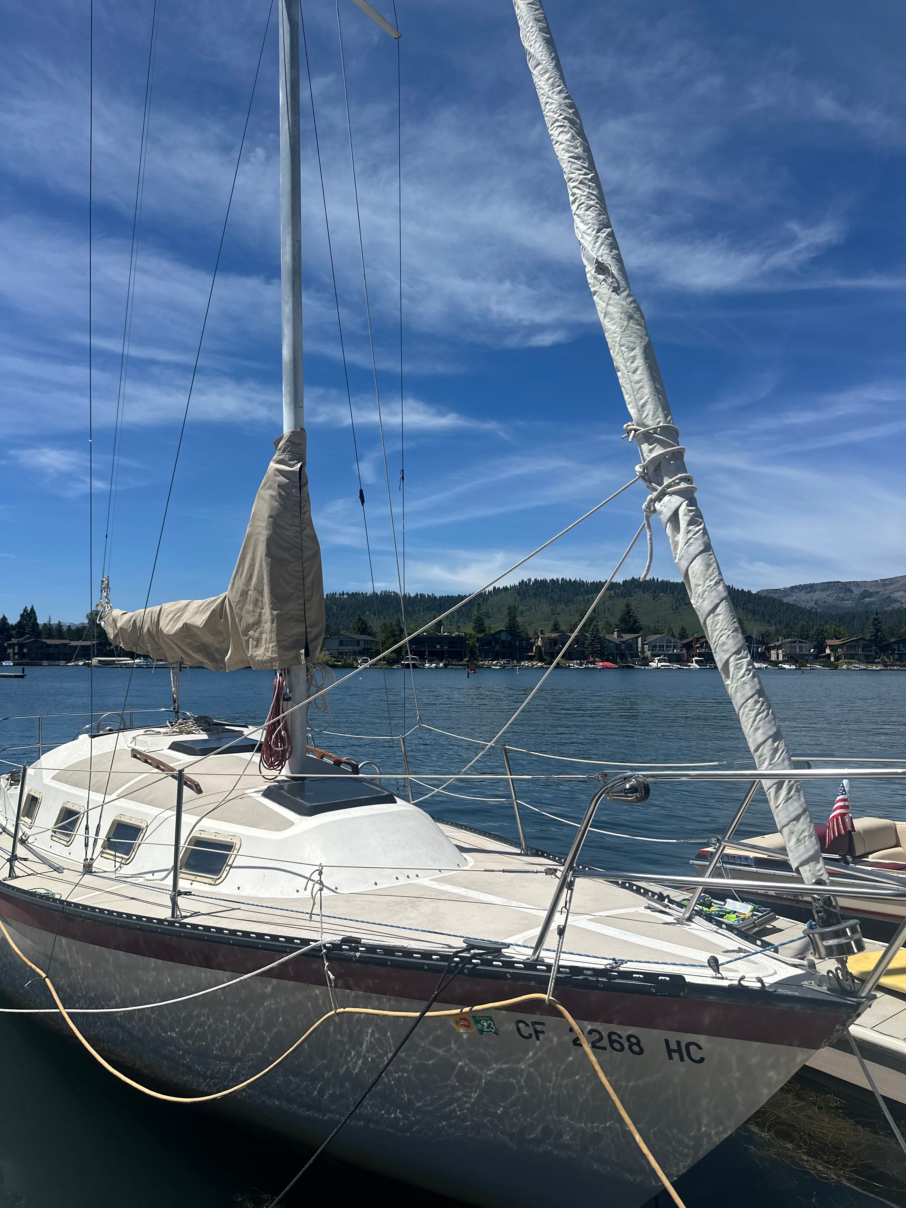 A 1982 Lancer 30 sailboat docked on a calm lake under a clear blue sky.