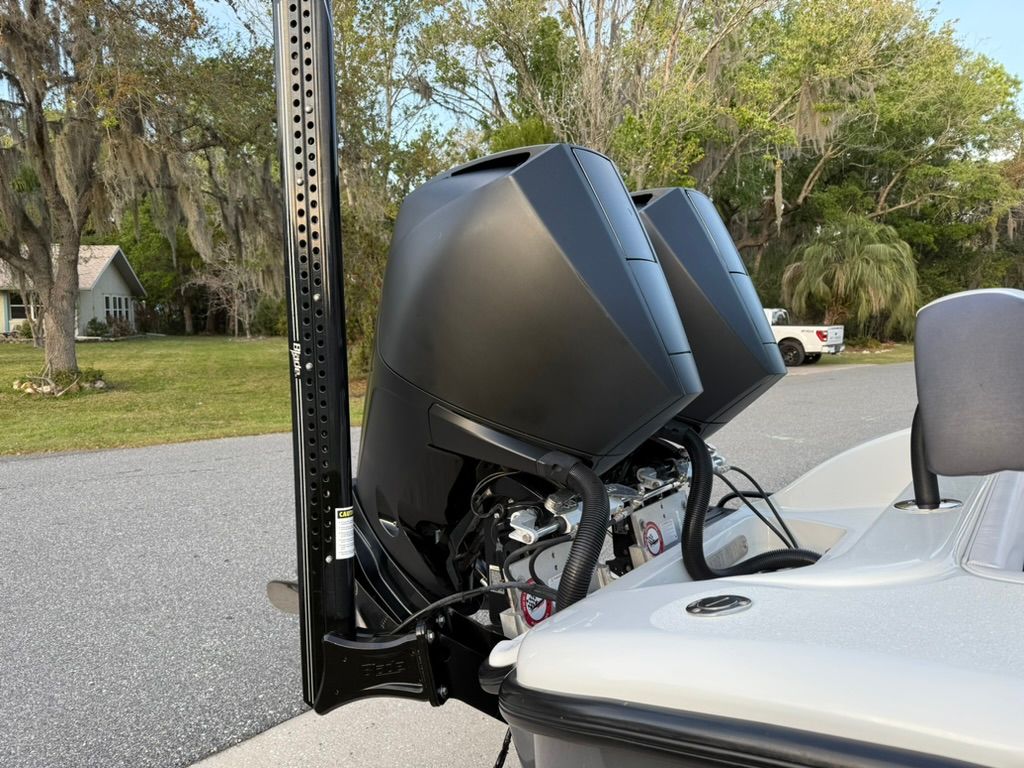 Two outboard motors on a boat parked in a lot, surrounded by trees.