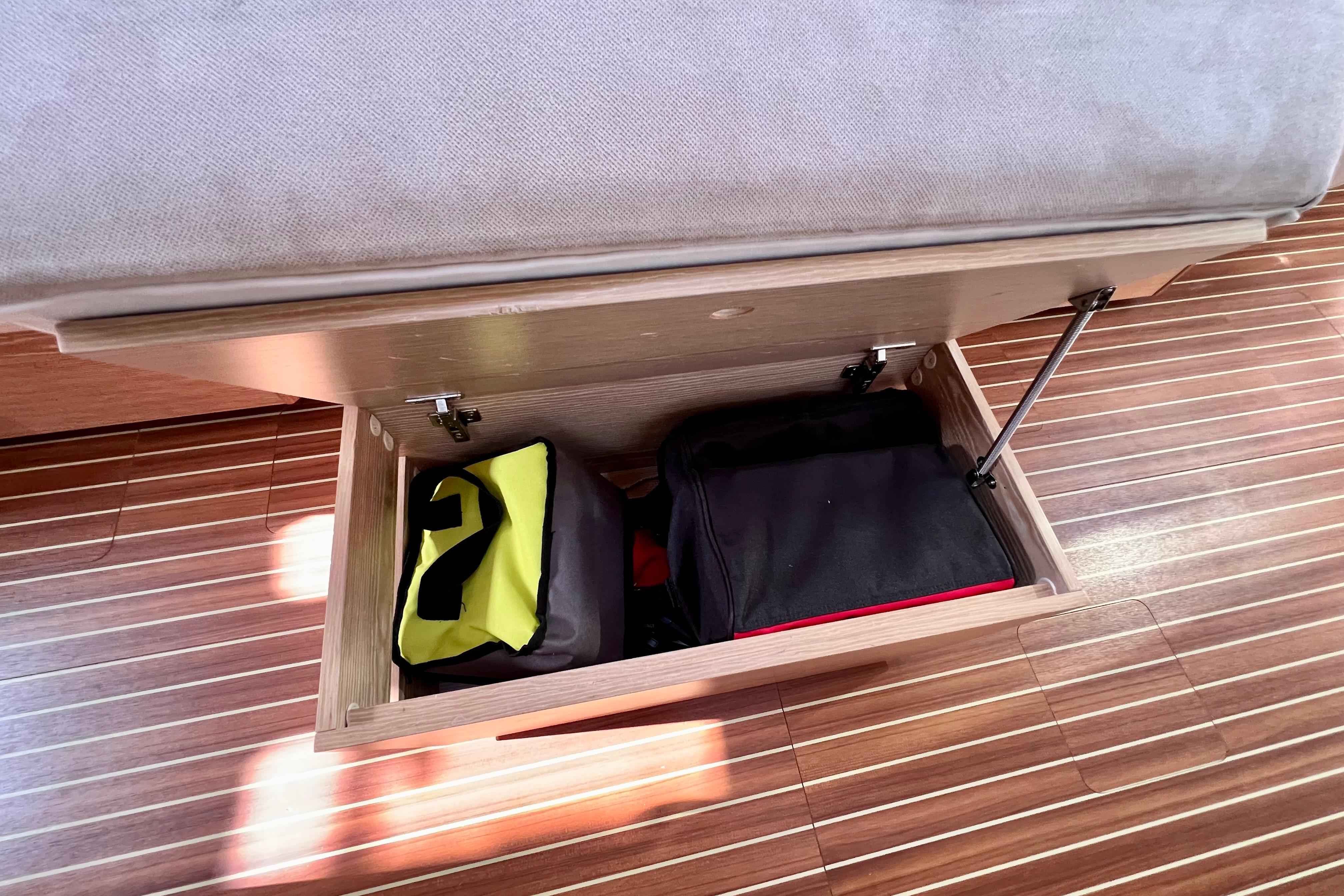 Storage compartment under seat in 2016 Hanse 455 yacht, containing bags on wooden flooring.