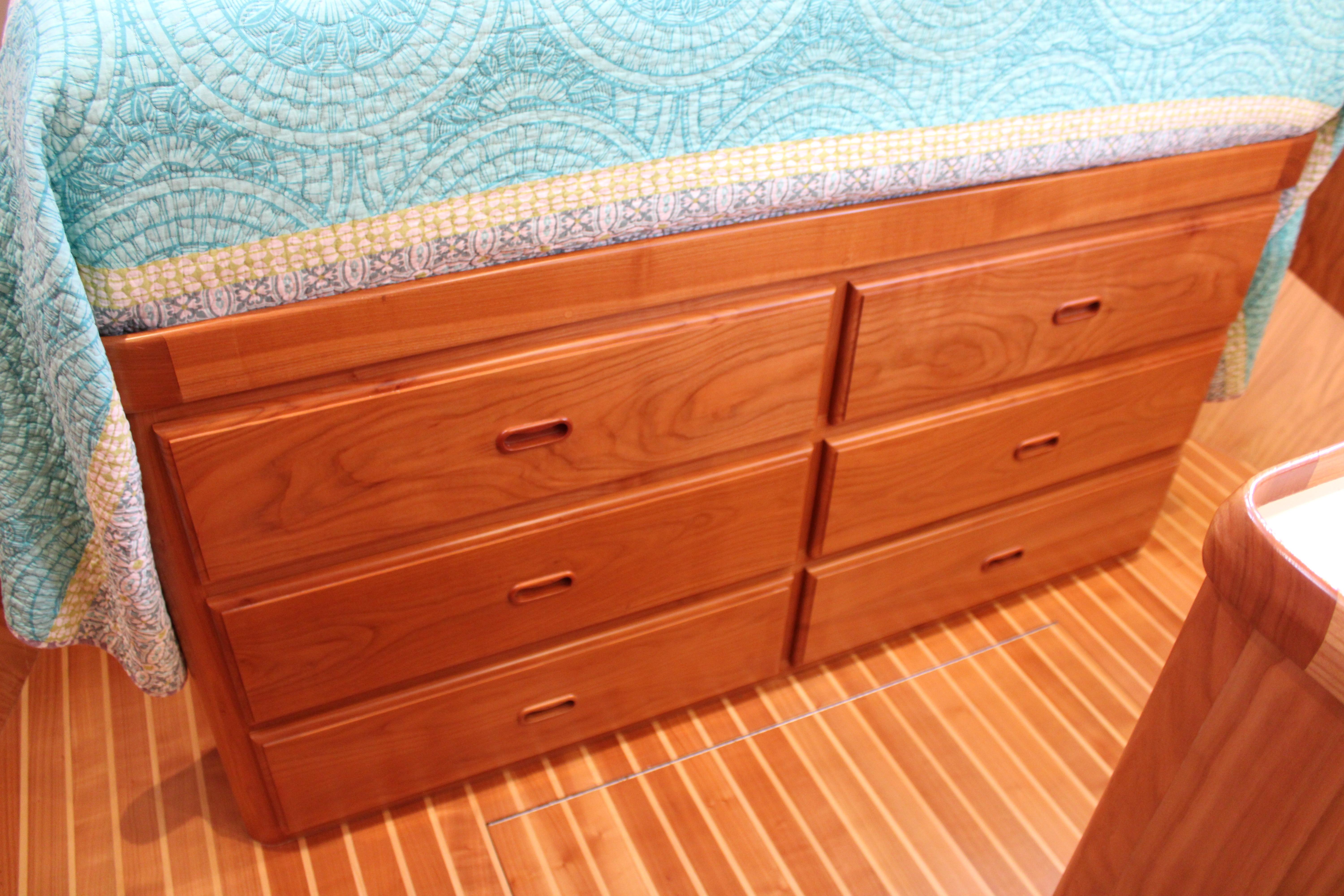 Wooden drawers under a bed with a quilt, aboard a 2023 Krogen Express 52' yacht.