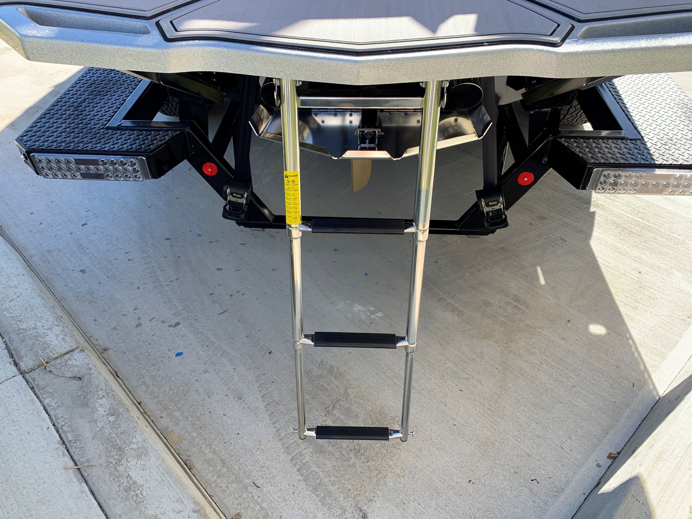 A swim ladder is attached to the stern of a boat, resting on a concrete surface.