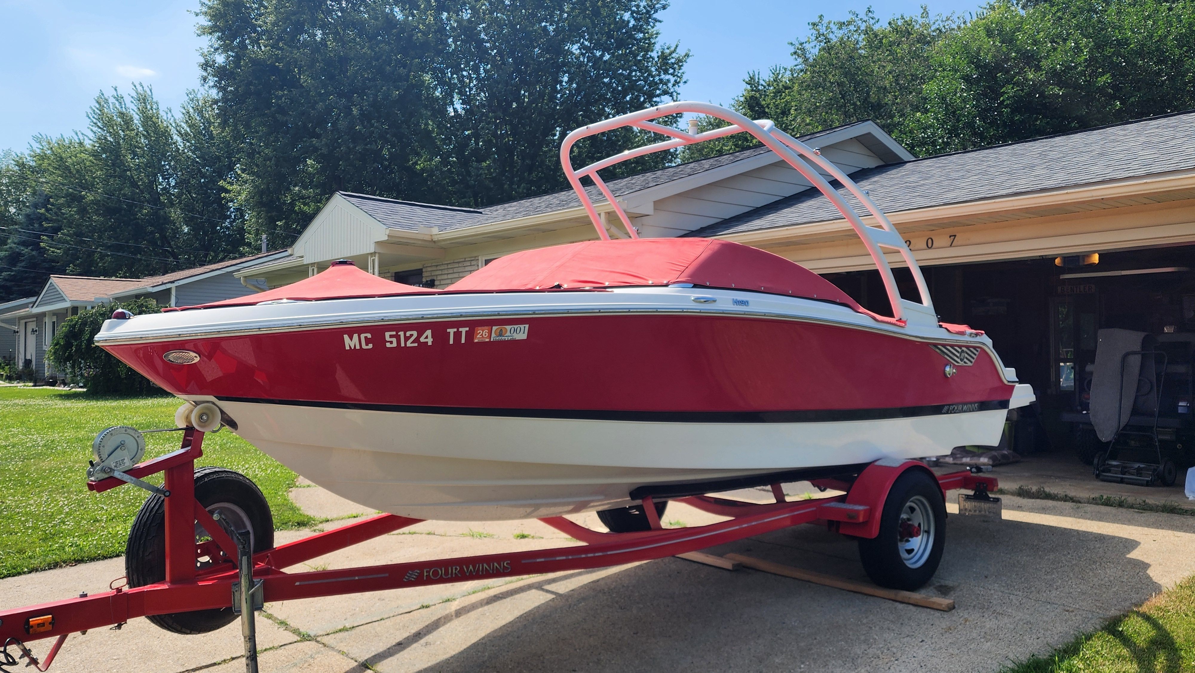 A red 2015 Four Winns H190 boat on a trailer in a driveway.