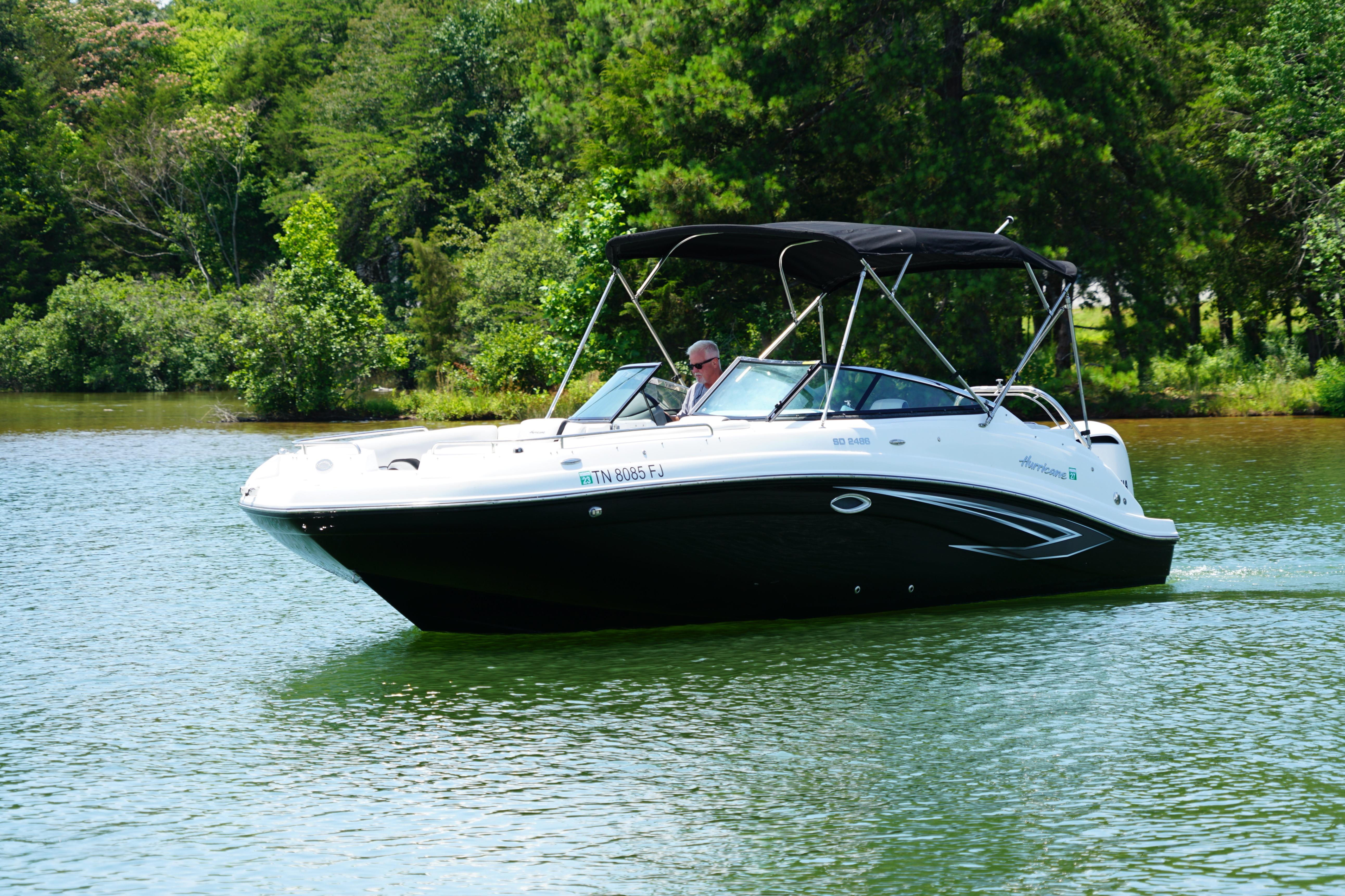 2020 Hurricane SunDeck 2486 OB boat cruising on a serene lake surrounded by lush greenery.