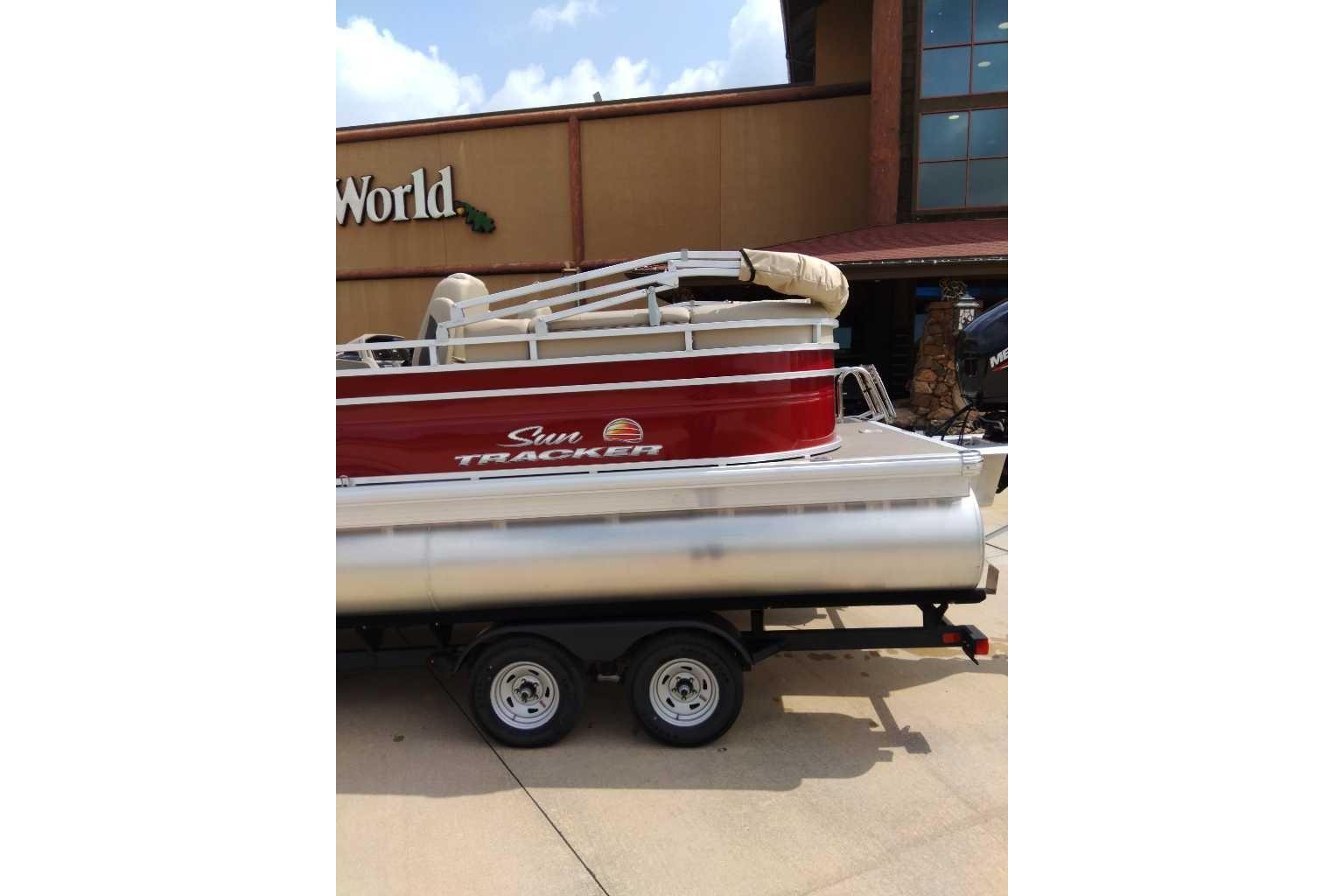 2025 Sun Tracker Party Barge 22 DLX pontoon boat on trailer, parked outside a store.