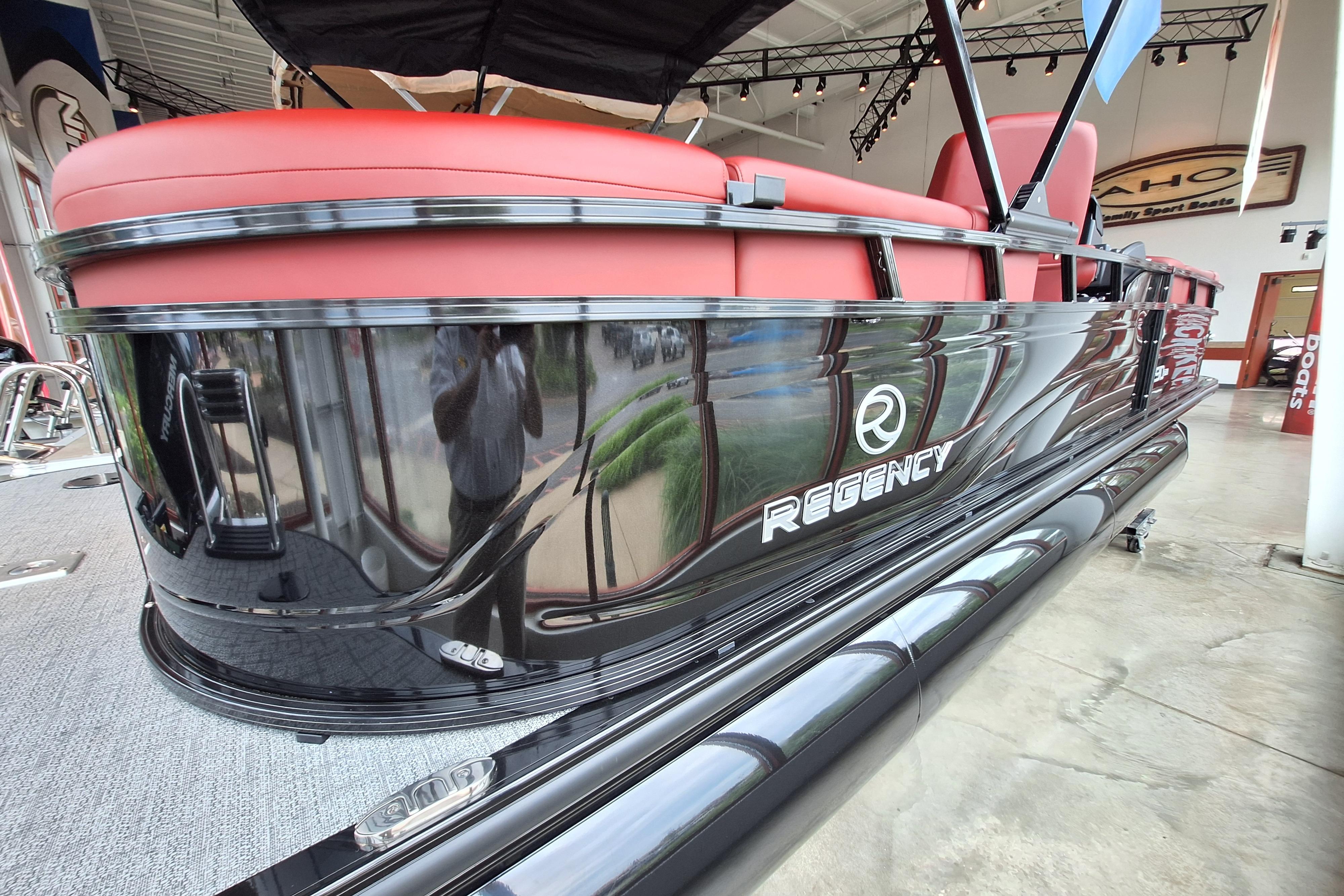 2026 Regency 230 DL pontoon boat with sleek black exterior and red seating in showroom.