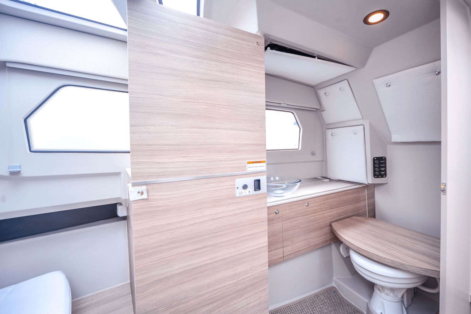 Interior of a modern boat cabin with toilet and sink, featuring light wood paneling.
