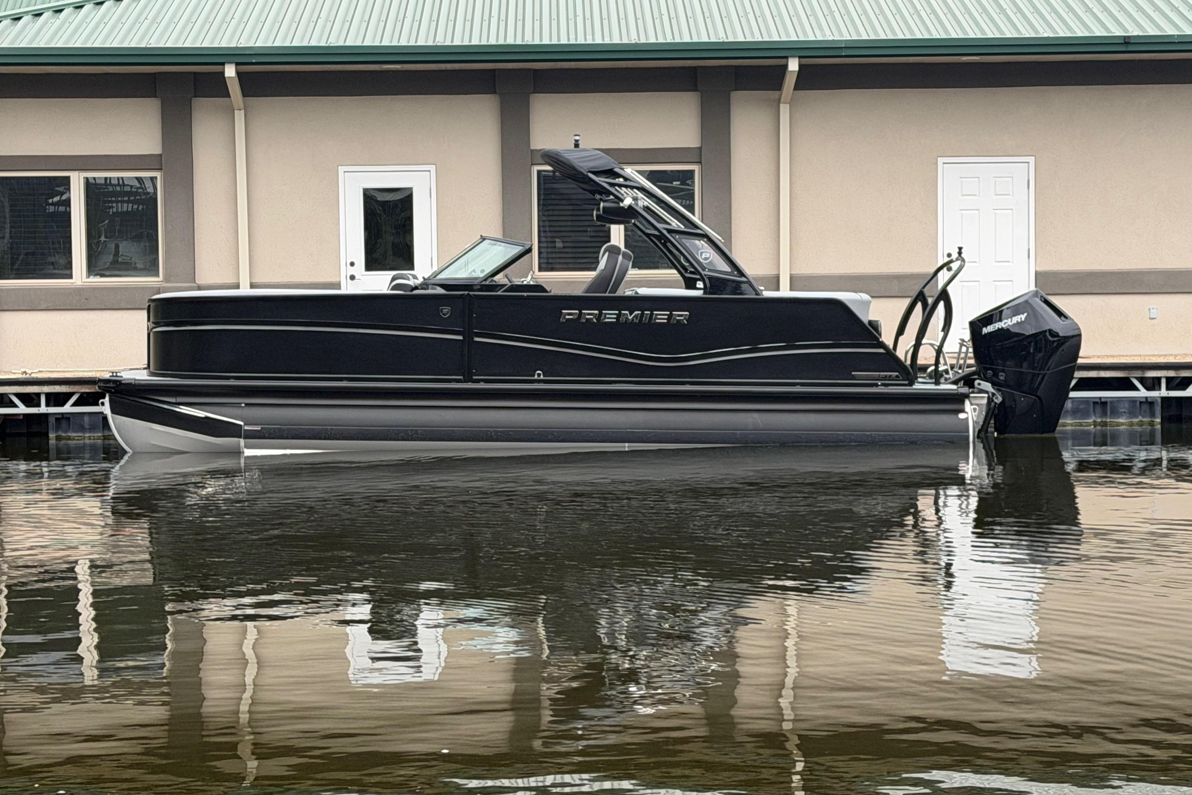 2026 Premier 250 Solaris Sport pontoon boat docked by a building.