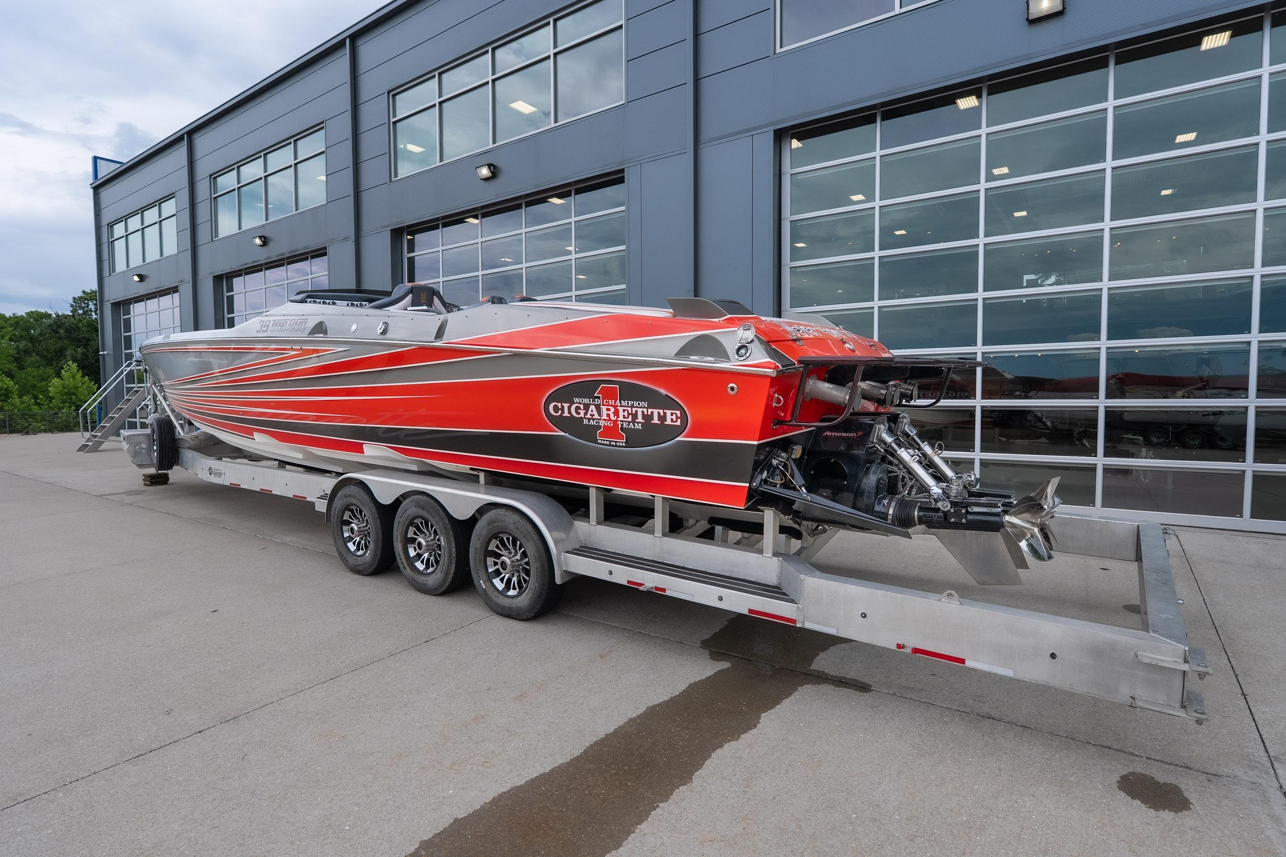 2006 Cigarette 39' Top Gun Unlimited boat on trailer, parked outside modern building.