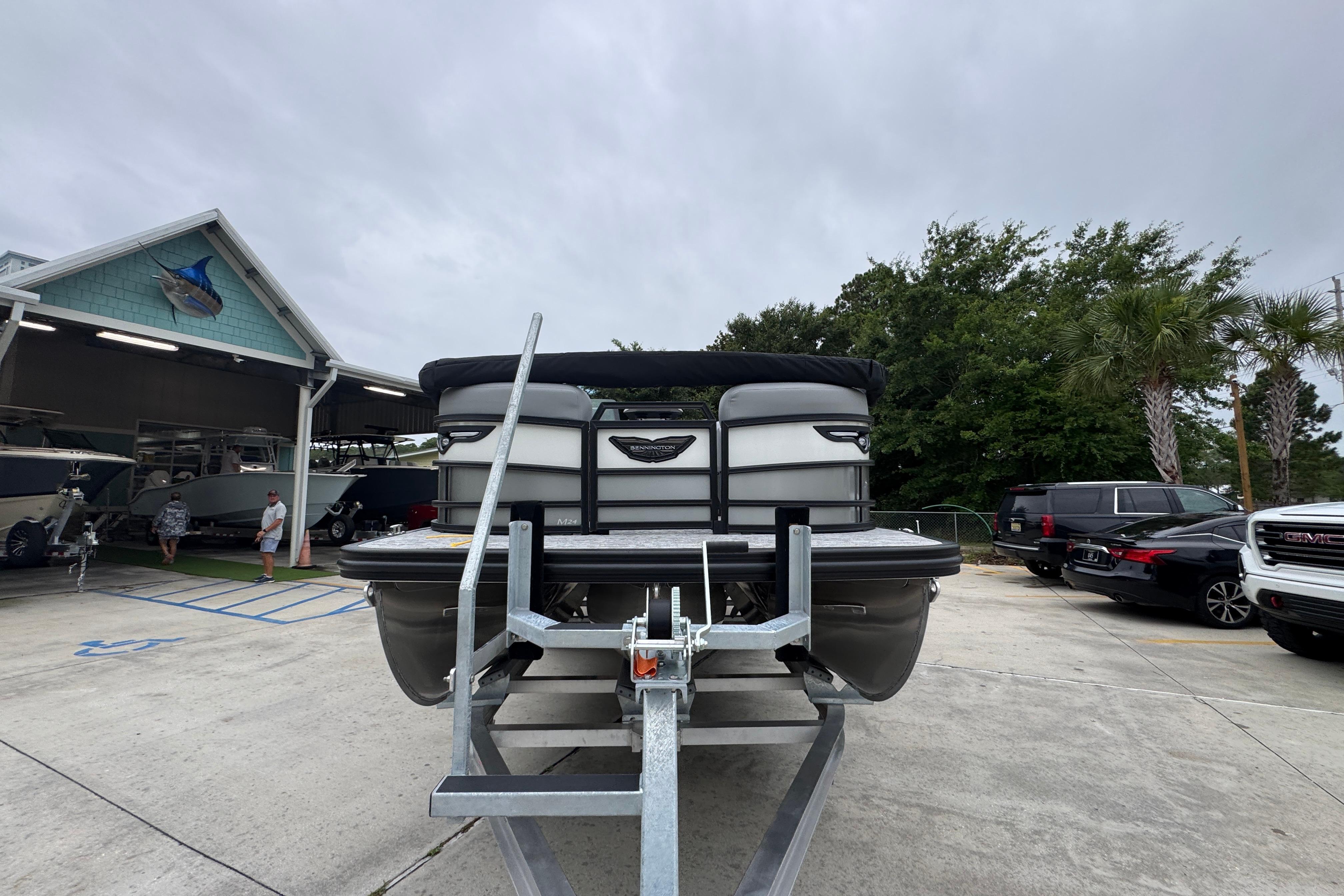 2027 Bennington 24 MFB pontoon boat on trailer at dealership, surrounded by cars and trees.
