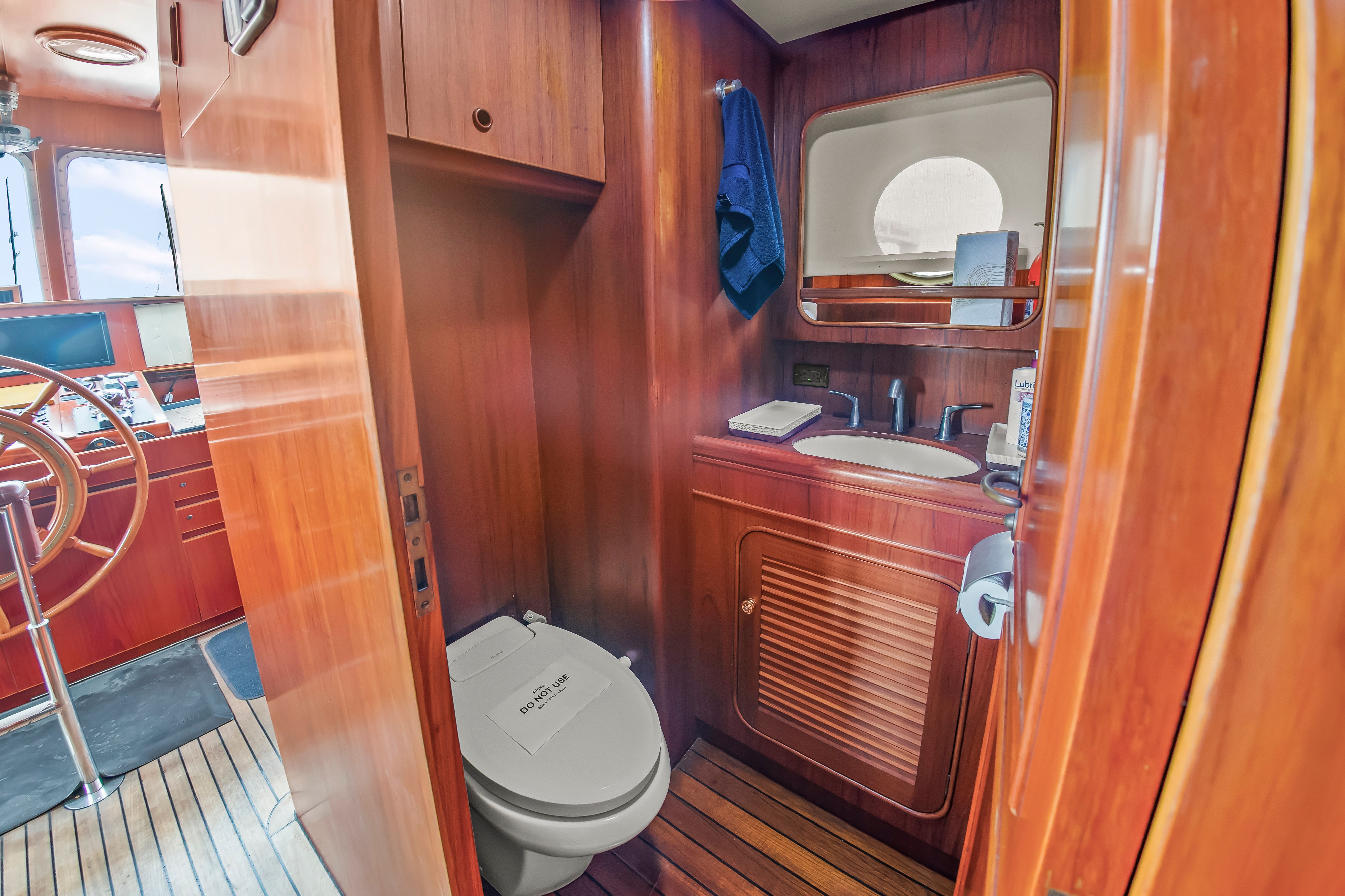 Interior of a yacht with wooden finish, sink, and toilet. A window provides natural light.