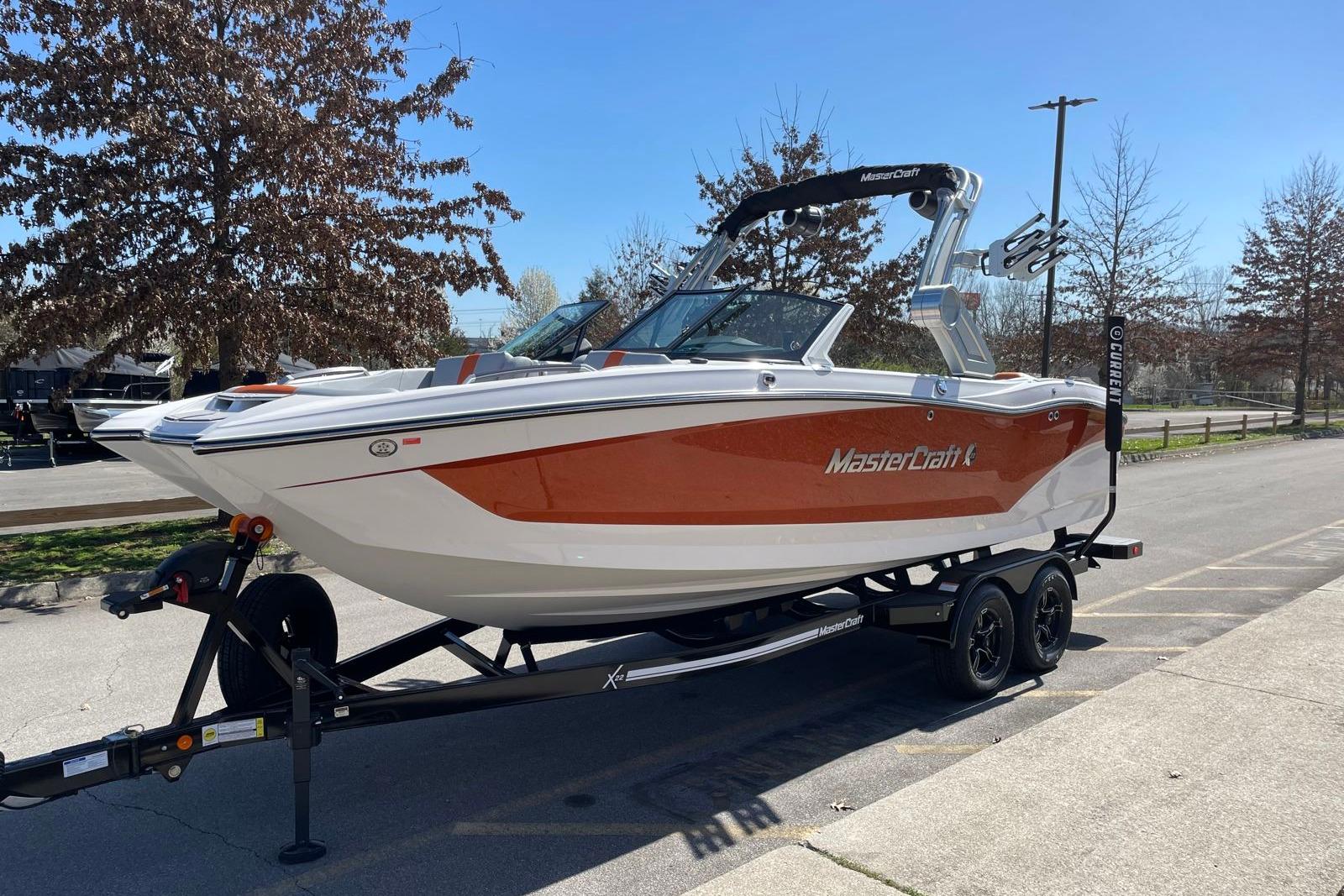 2024 MasterCraft X22 boat on trailer, parked outdoors, showcasing sleek design and vibrant colors.
