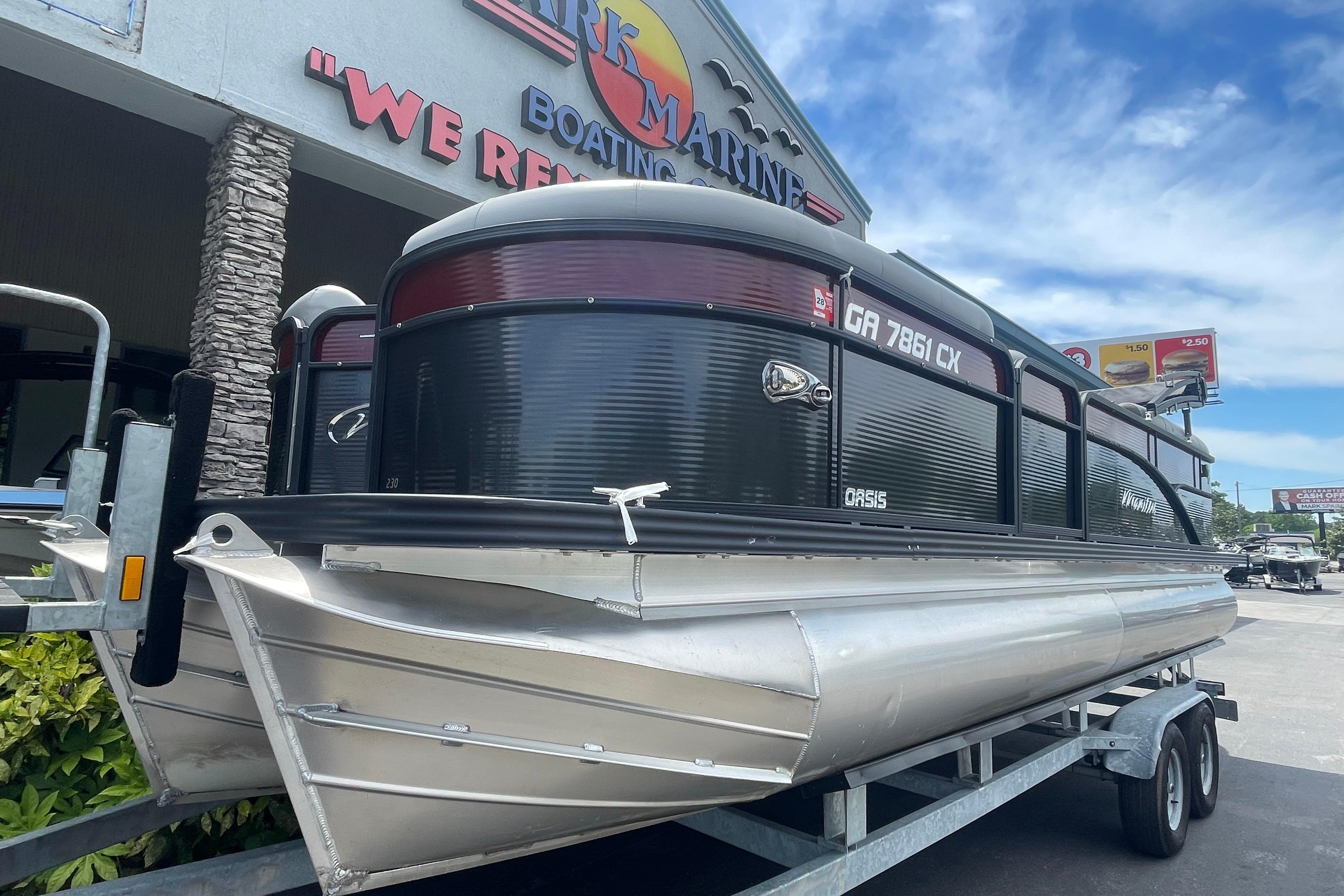 2022 Manitou 23 Oasis pontoon boat on trailer at dealership under blue sky.