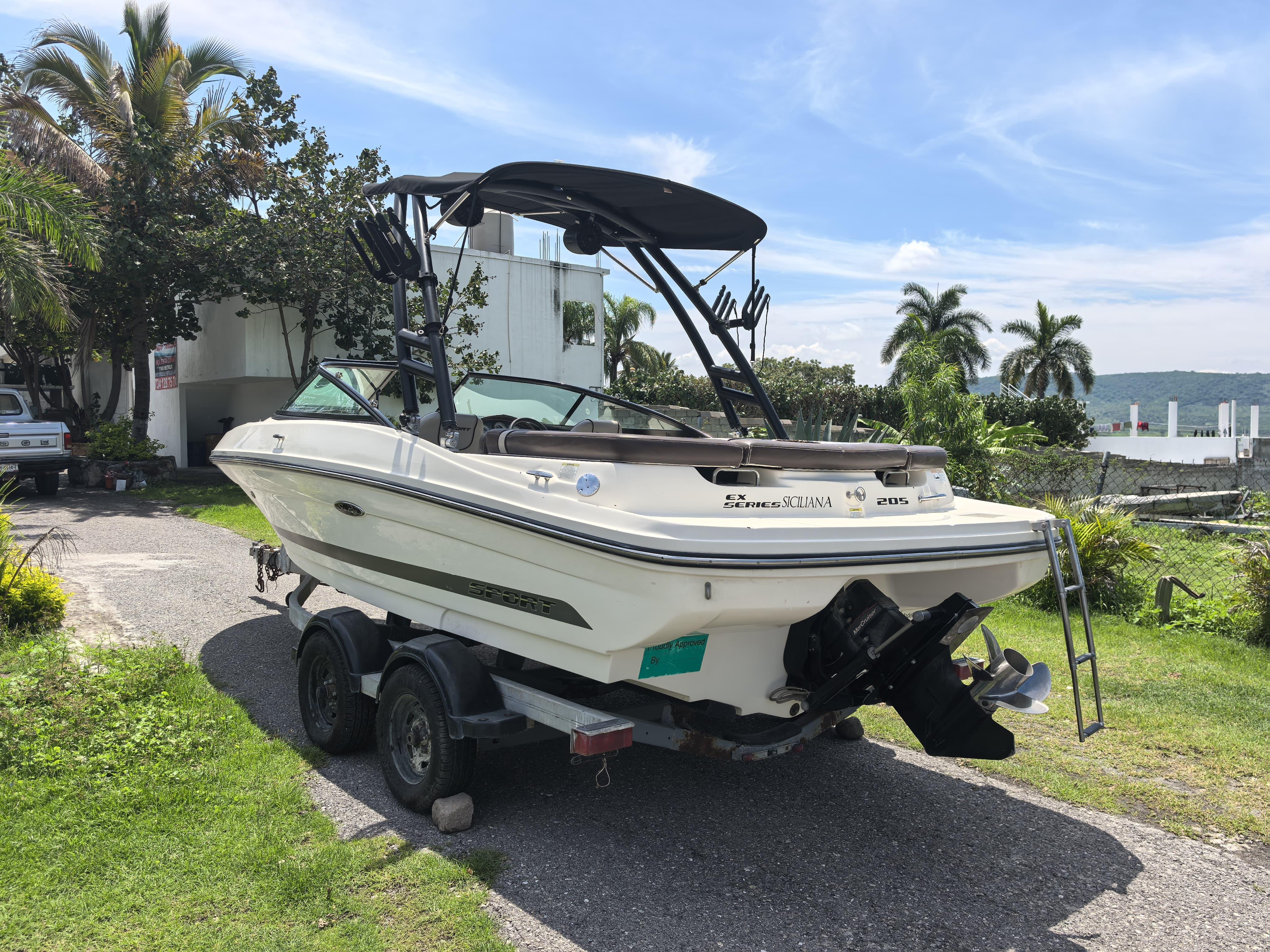 2013 Sea Ray 205 Sport boat on trailer, parked near tropical landscape.
