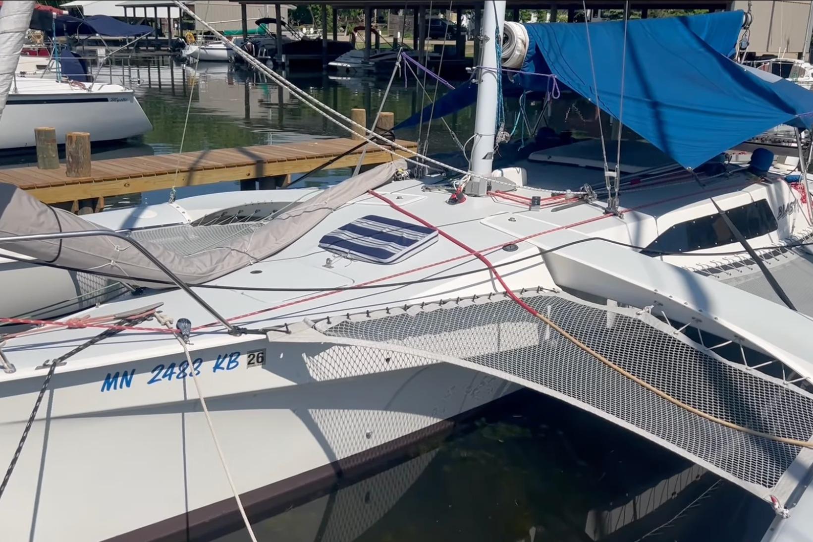 1993 Corsair F-27 trimaran docked at marina, featuring blue tarp and netting.