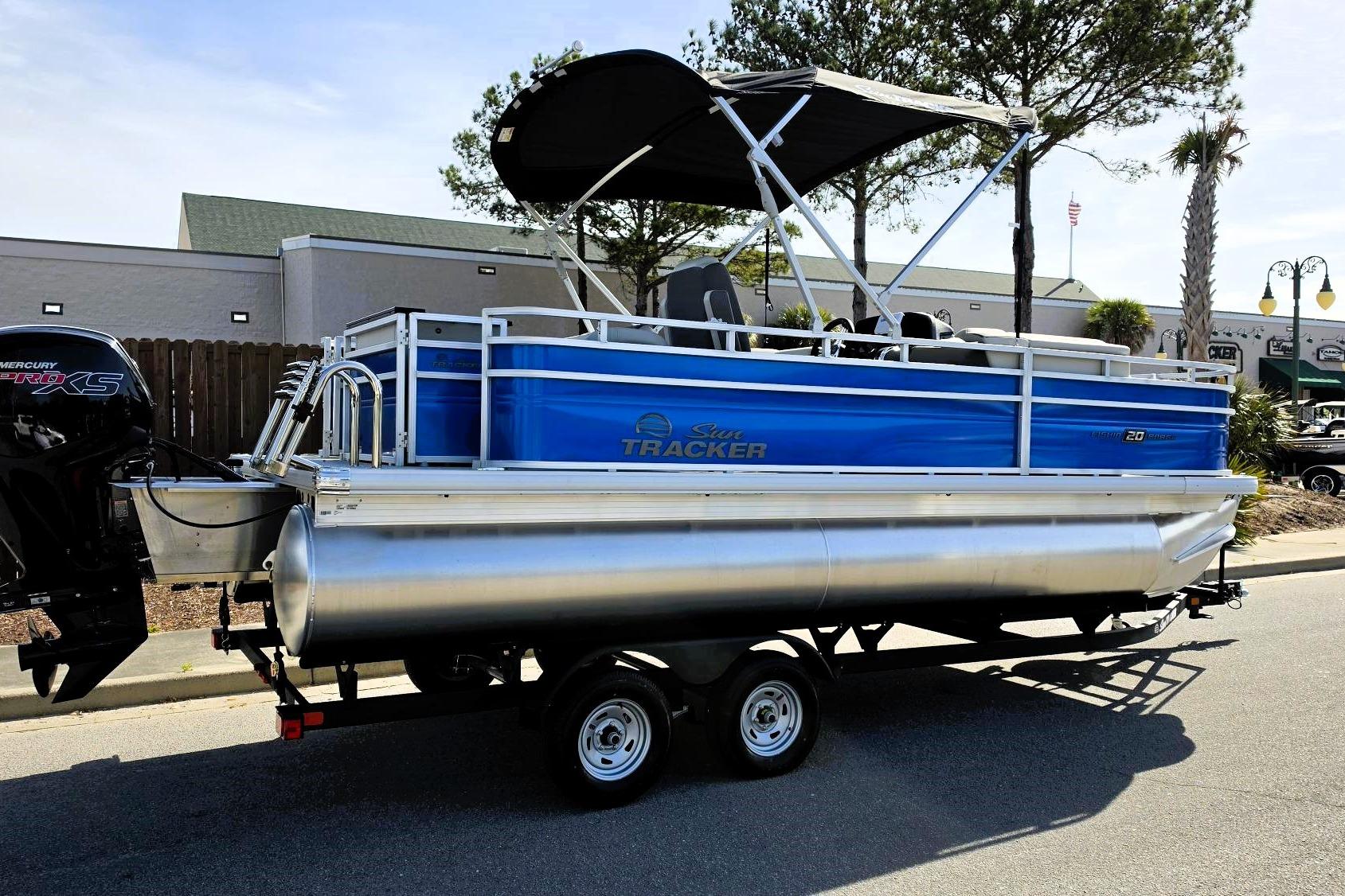 2026 Sun Tracker Fishin' Barge 20 DLX pontoon boat on trailer, blue and silver design.