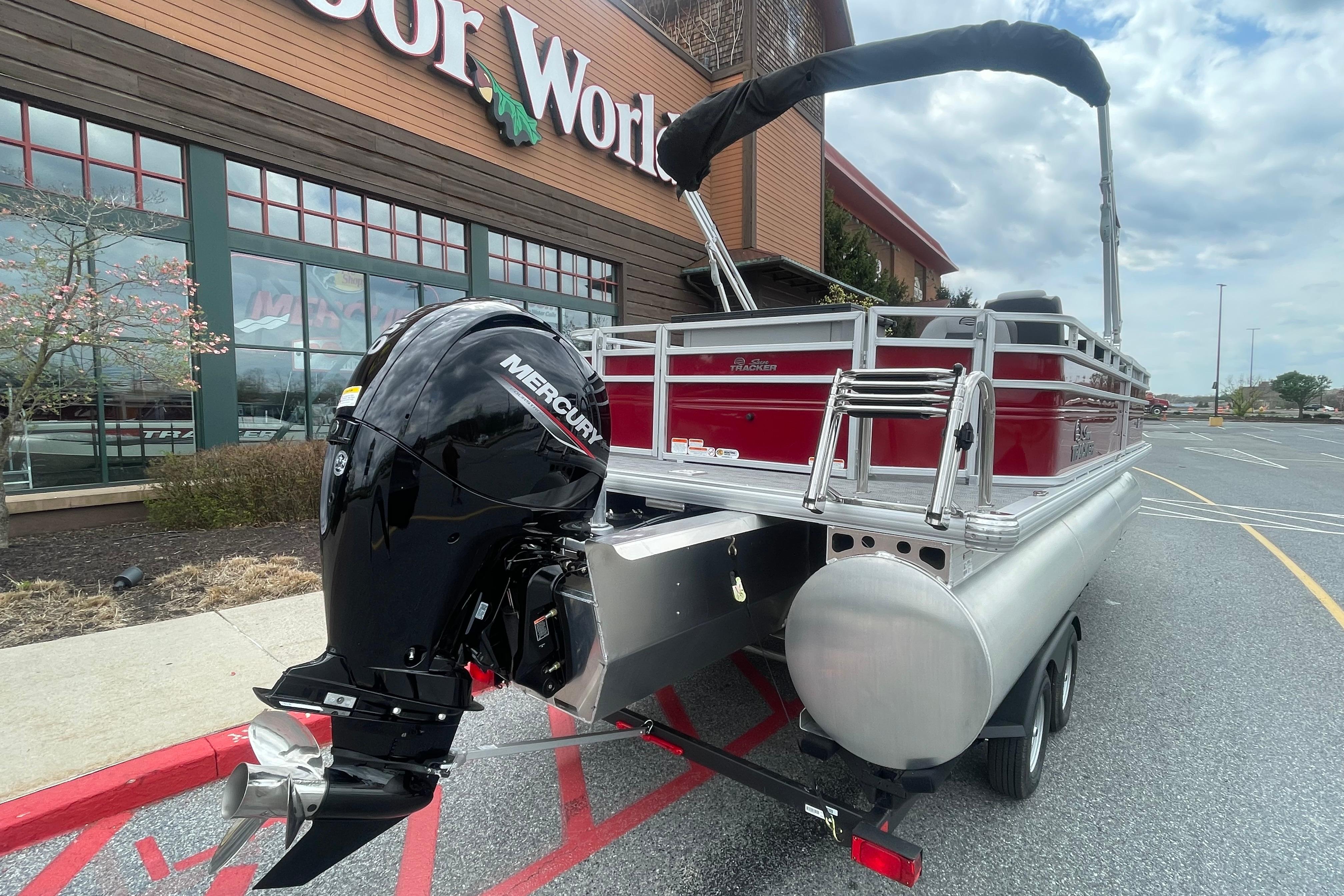 2026 Sun Tracker SportFish 22 XP3 pontoon boat with Mercury engine, parked outside a store.