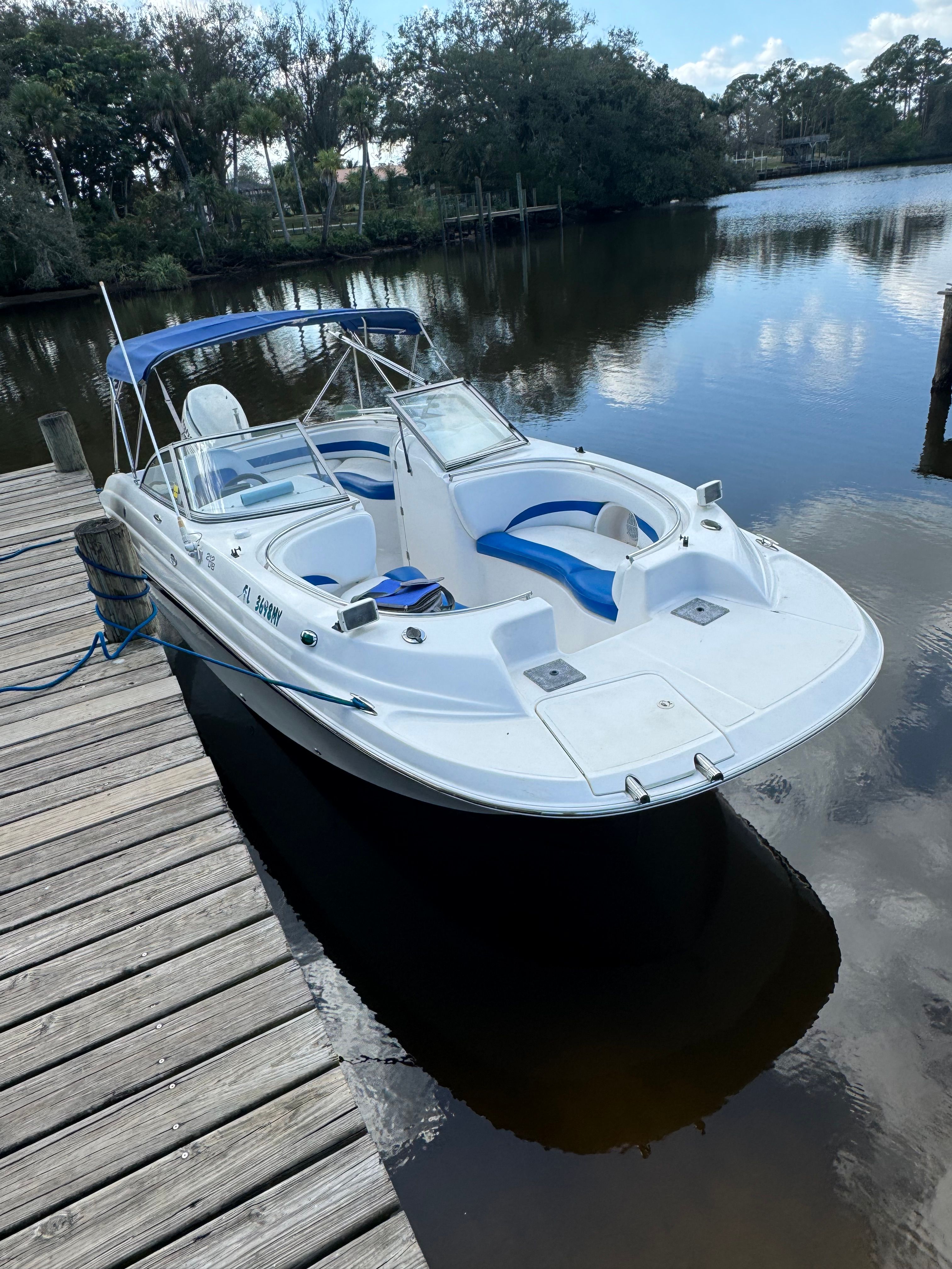 A white boat with blue accents is docked at a wooden pier in calm water.