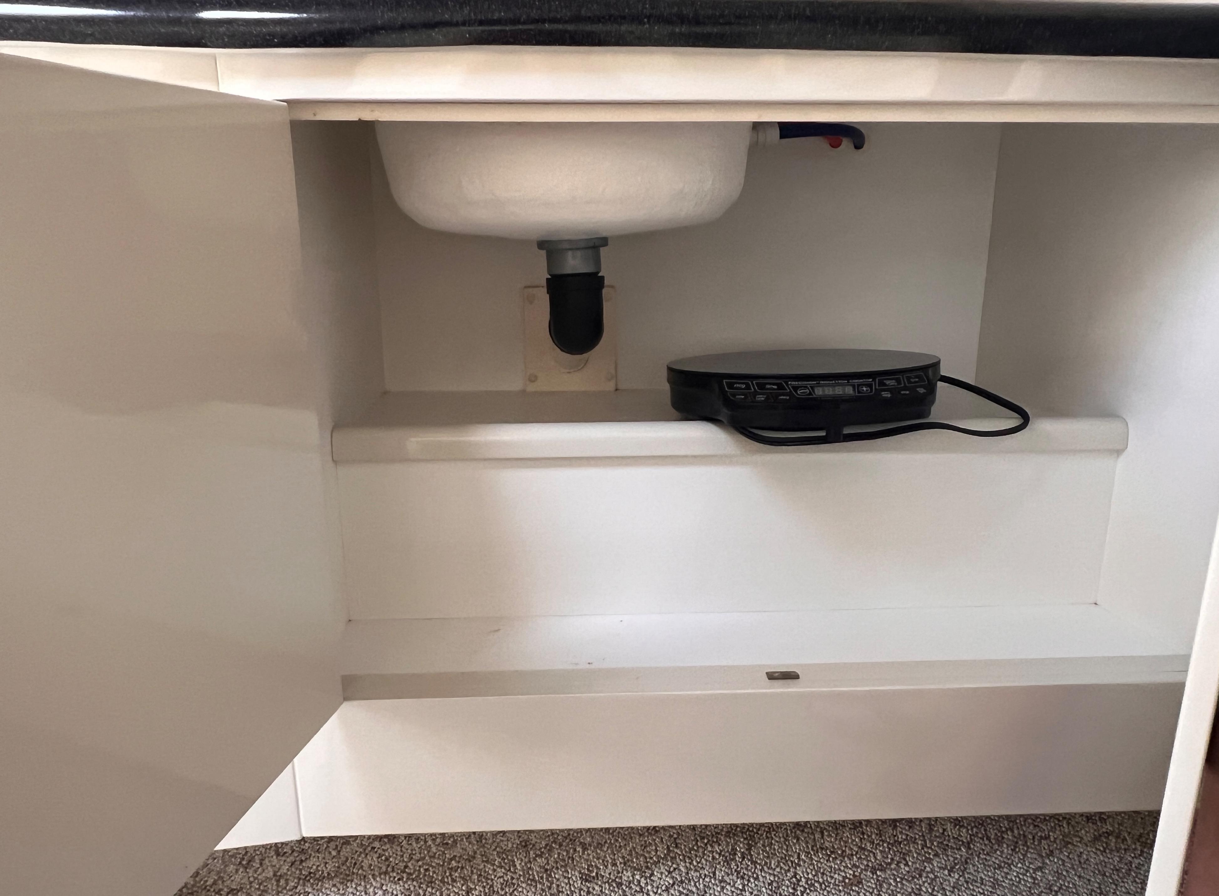 Under-sink storage in 2000 Wellcraft 45 Excalibur boat, featuring plumbing and electronic device.