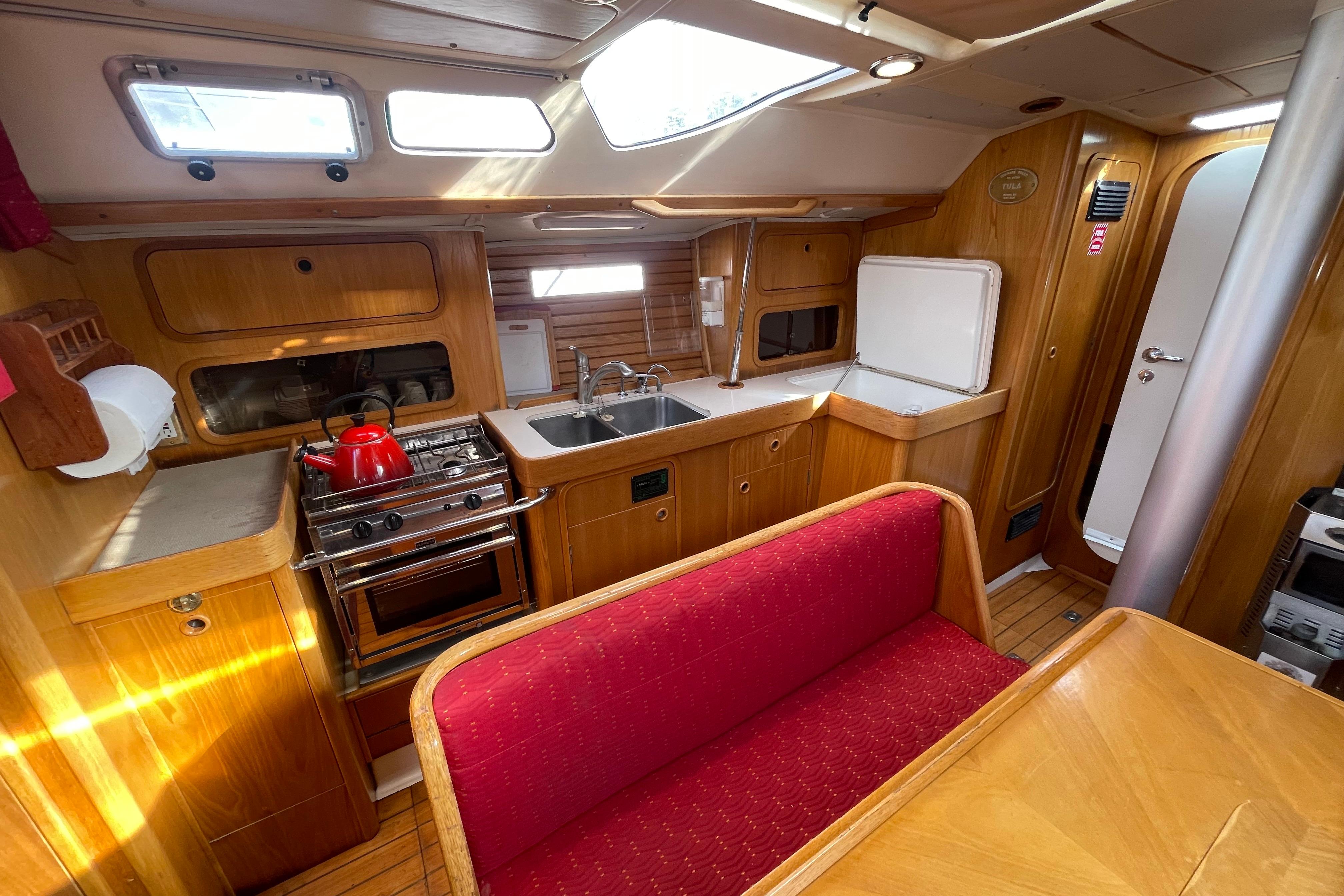 Cozy 1990 Beneteau Oceanis 390 yacht interior with wooden cabinetry and red seating.