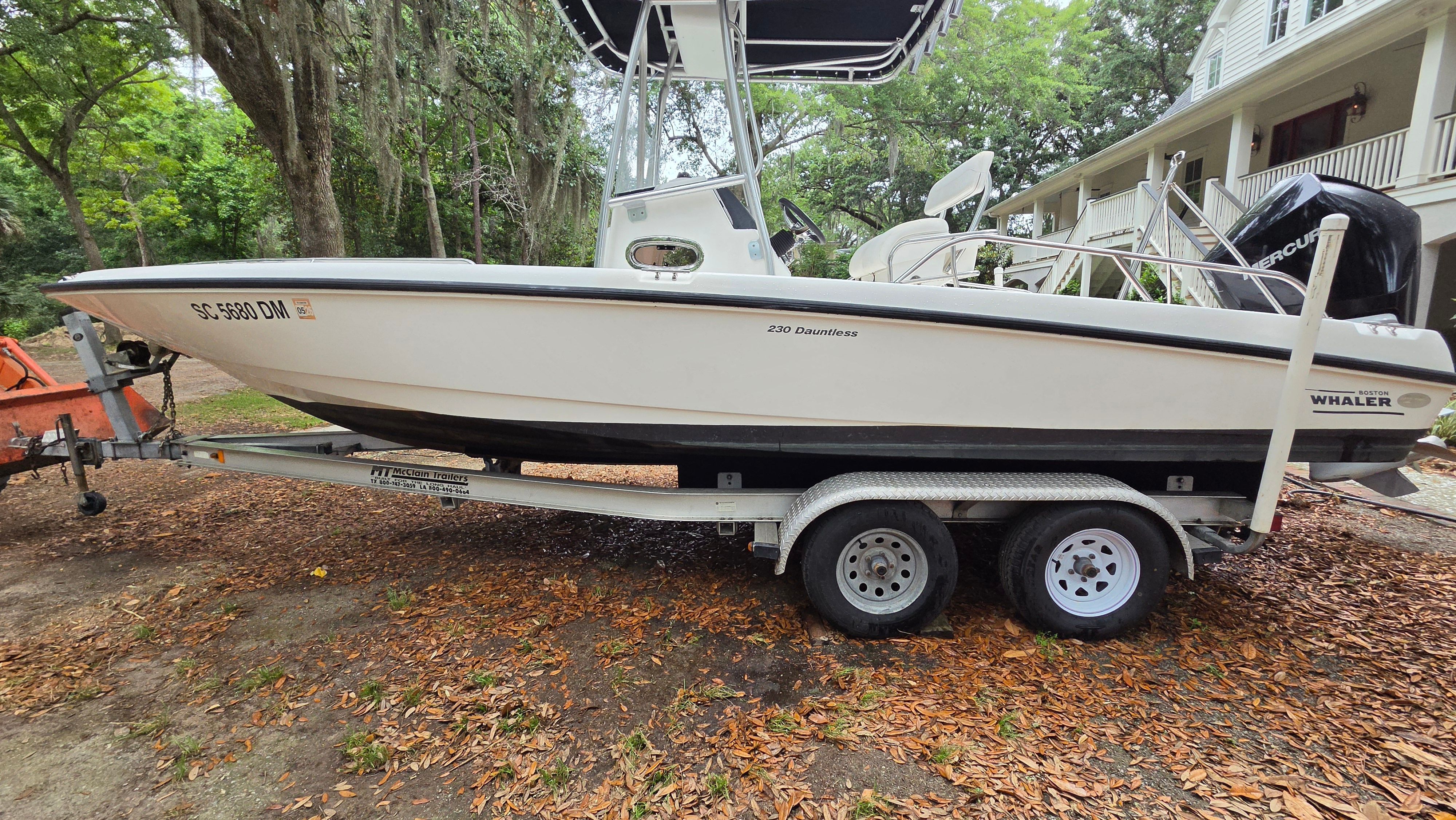 A 2008 Boston Whaler 230 Dauntless on a trailer, surrounded by leaves and trees.