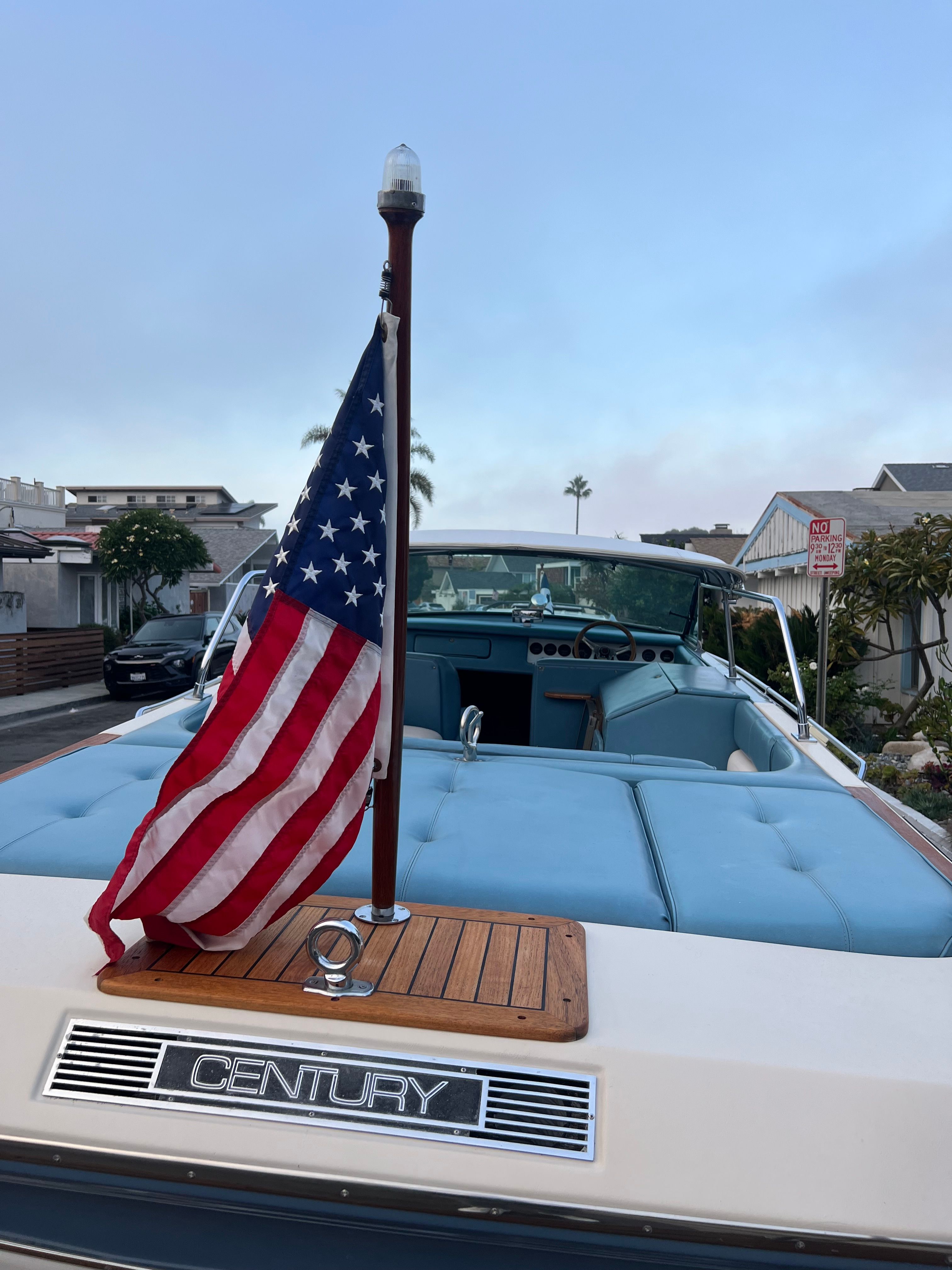 1985 Century Coronado Cardel boat with American flag, blue interior, parked in residential area.