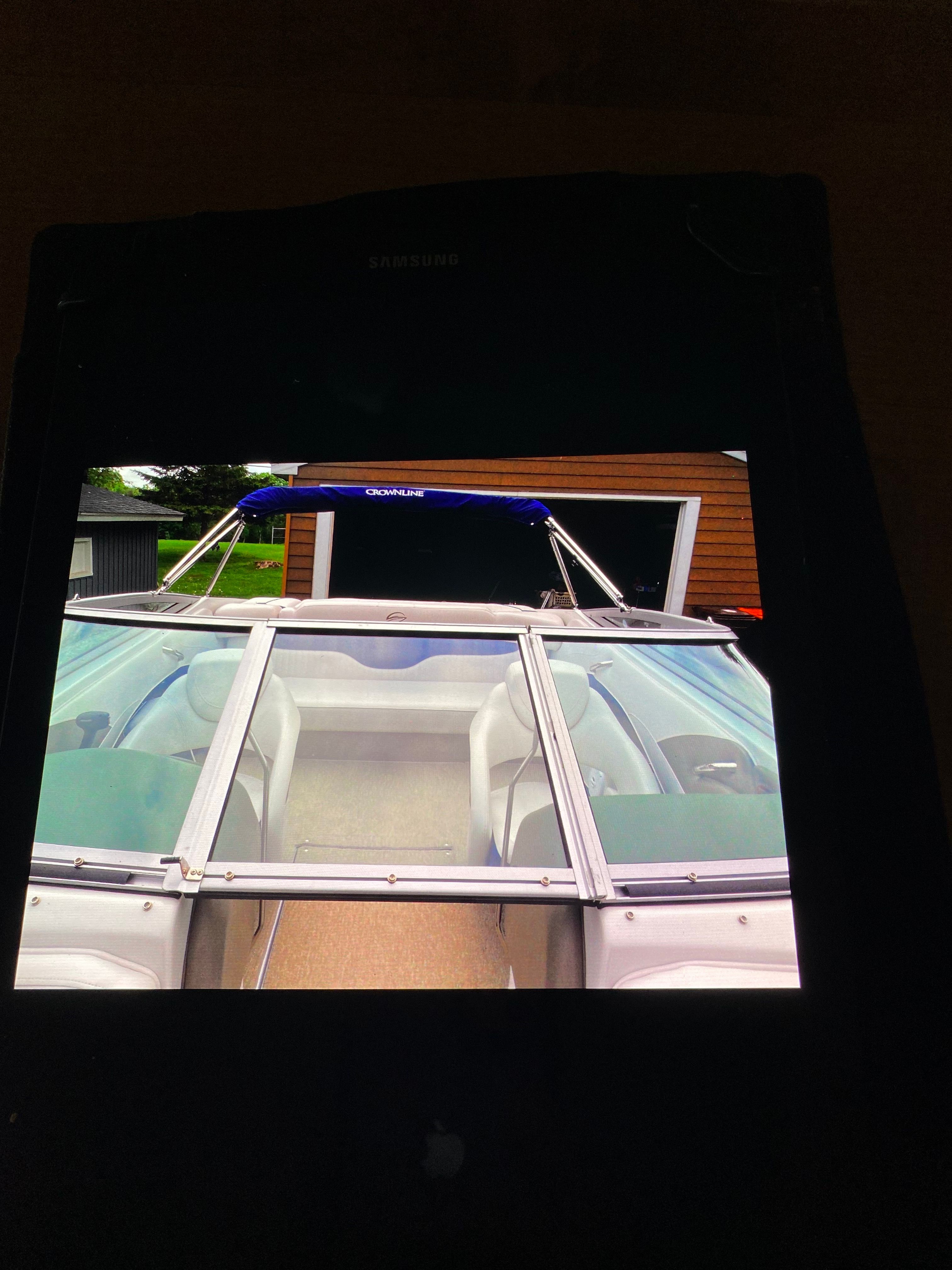 A Crownline 21 bowrider boat with a blue canopy, parked in front of a building.