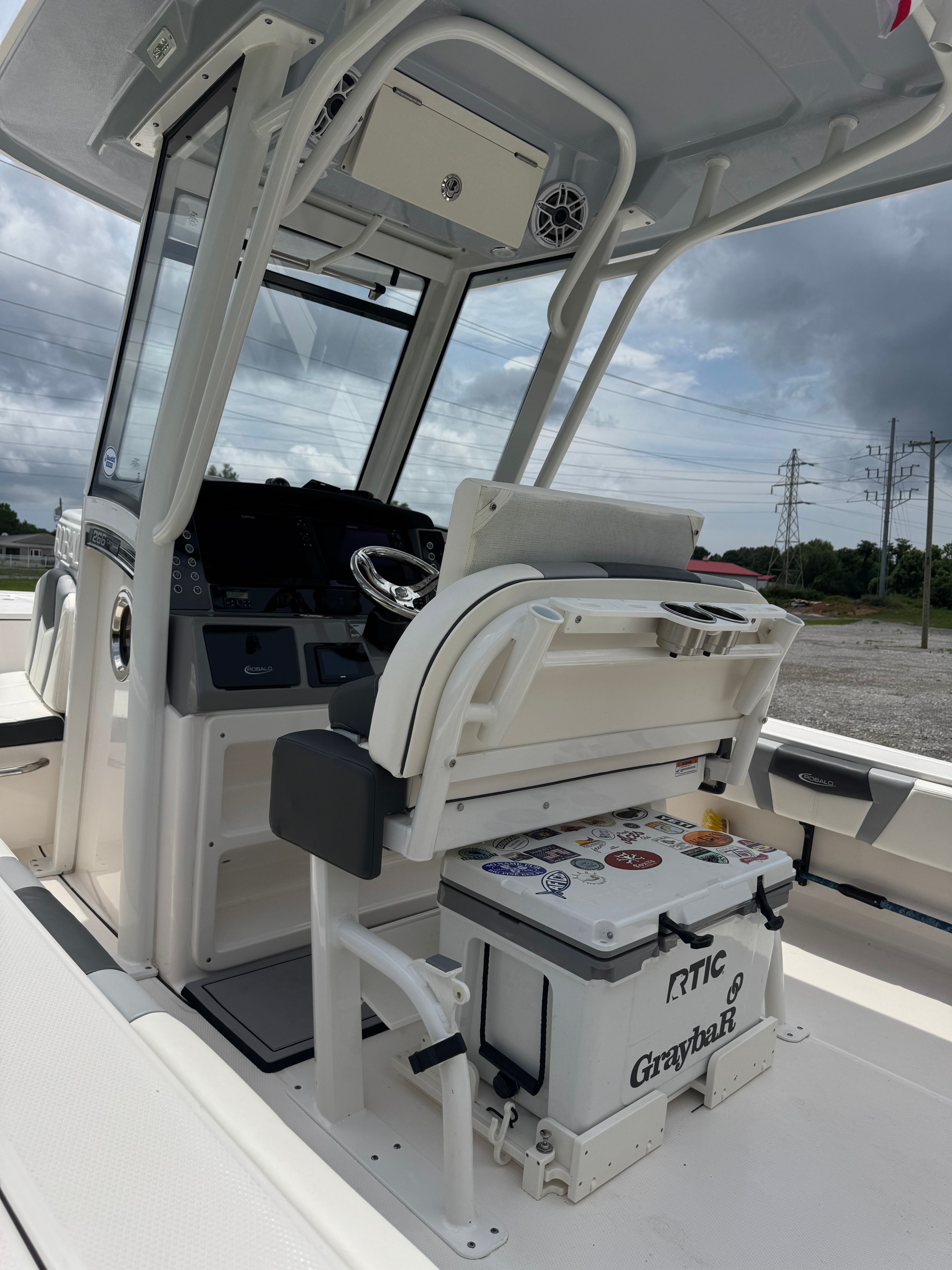 The image shows the cockpit of a 2023 Robalo 266 Cayman boat with helm and cooler.