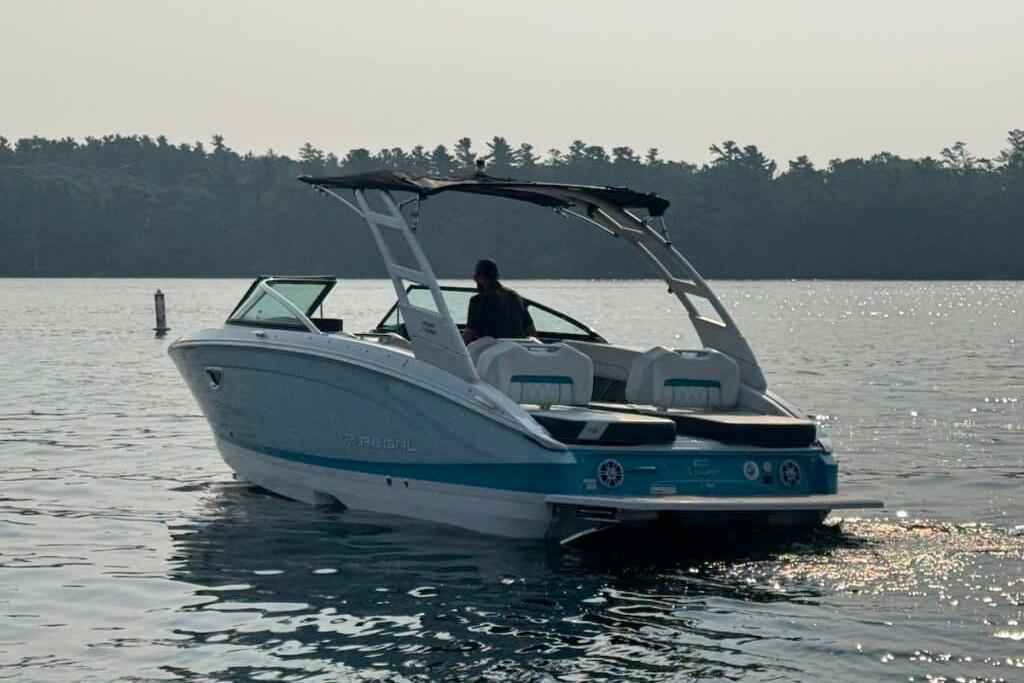 2022 Regal LS6 Surf boat cruising on a calm lake with forested shoreline.