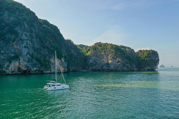 Sailing Lagoon 42 Millenium catamaran in serene turquoise waters near lush cliffs, 2025 model.