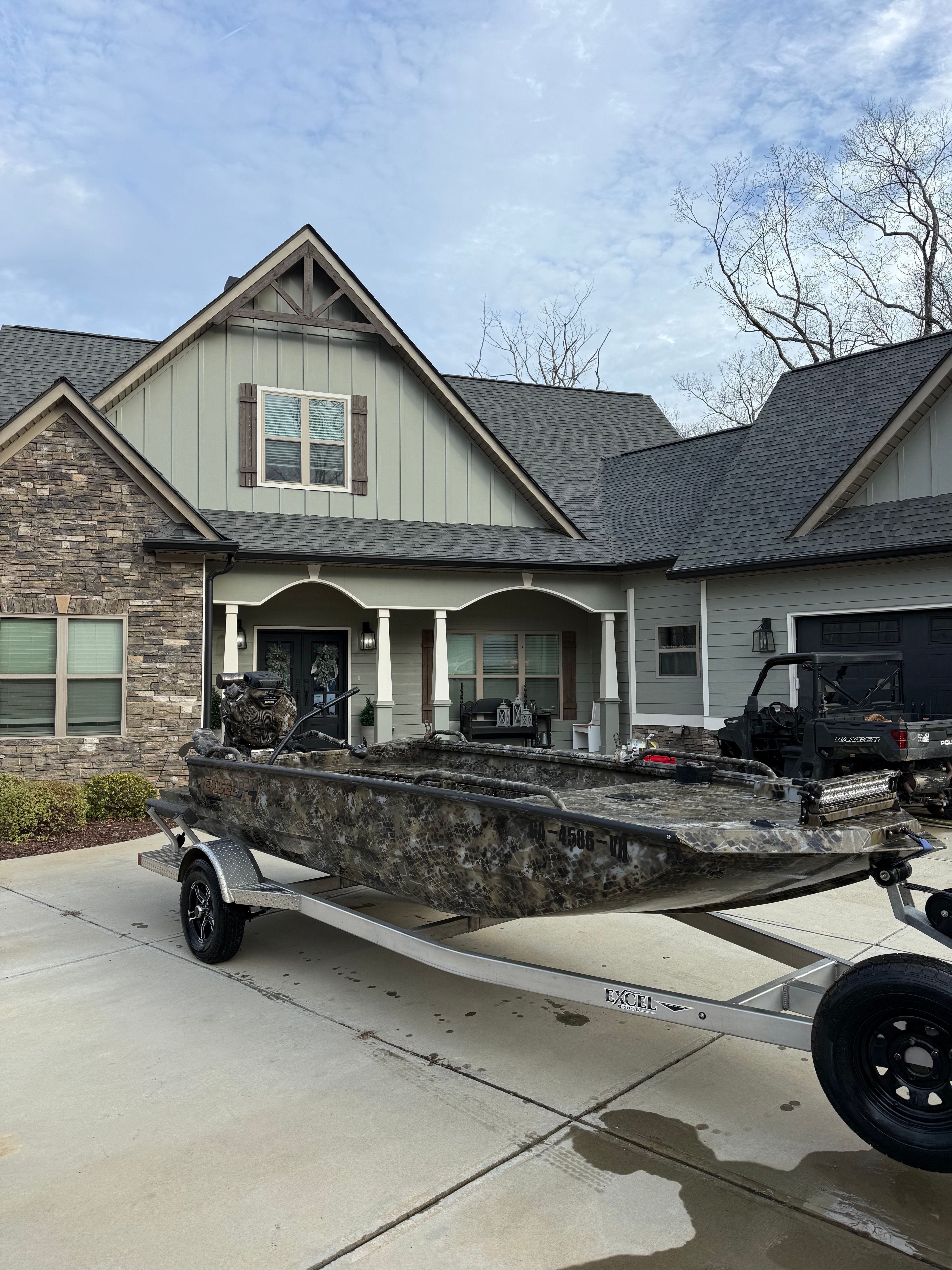 2024 Excel 1754 Shallow Water F4 boat parked in front of a modern house.