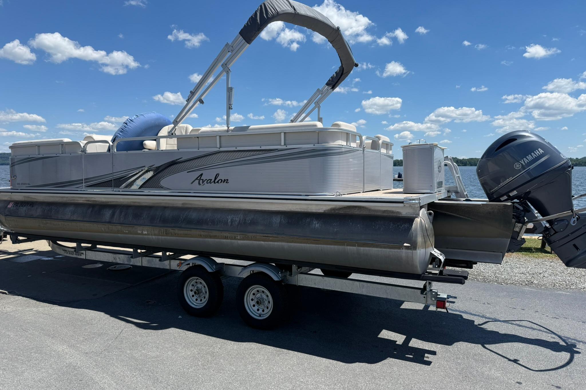 2019 Avalon GS Quad Lounge 25' pontoon boat on trailer by a lake under blue sky.