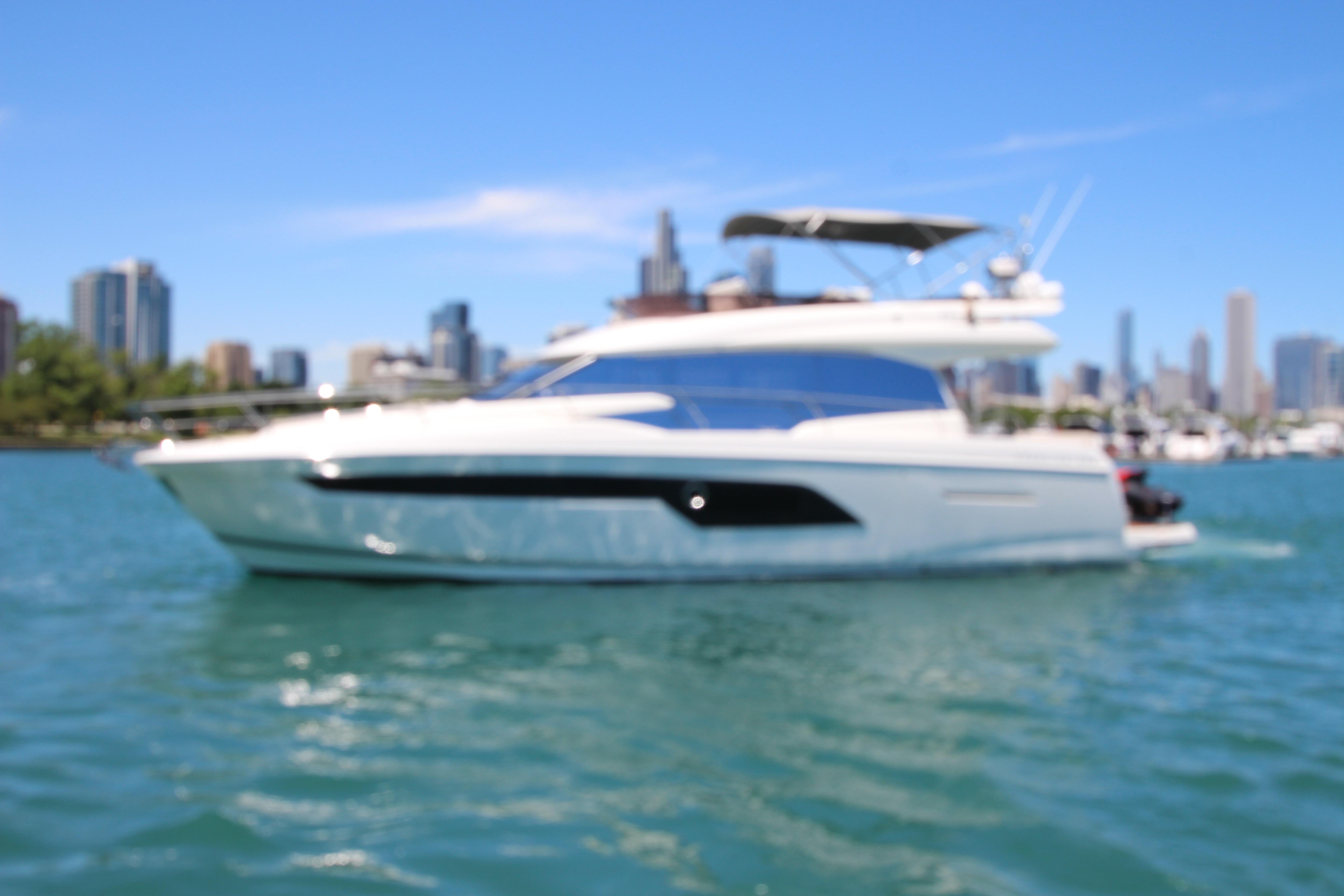 Blurry image of a 2022 Prestige 520 yacht on water with city skyline background.