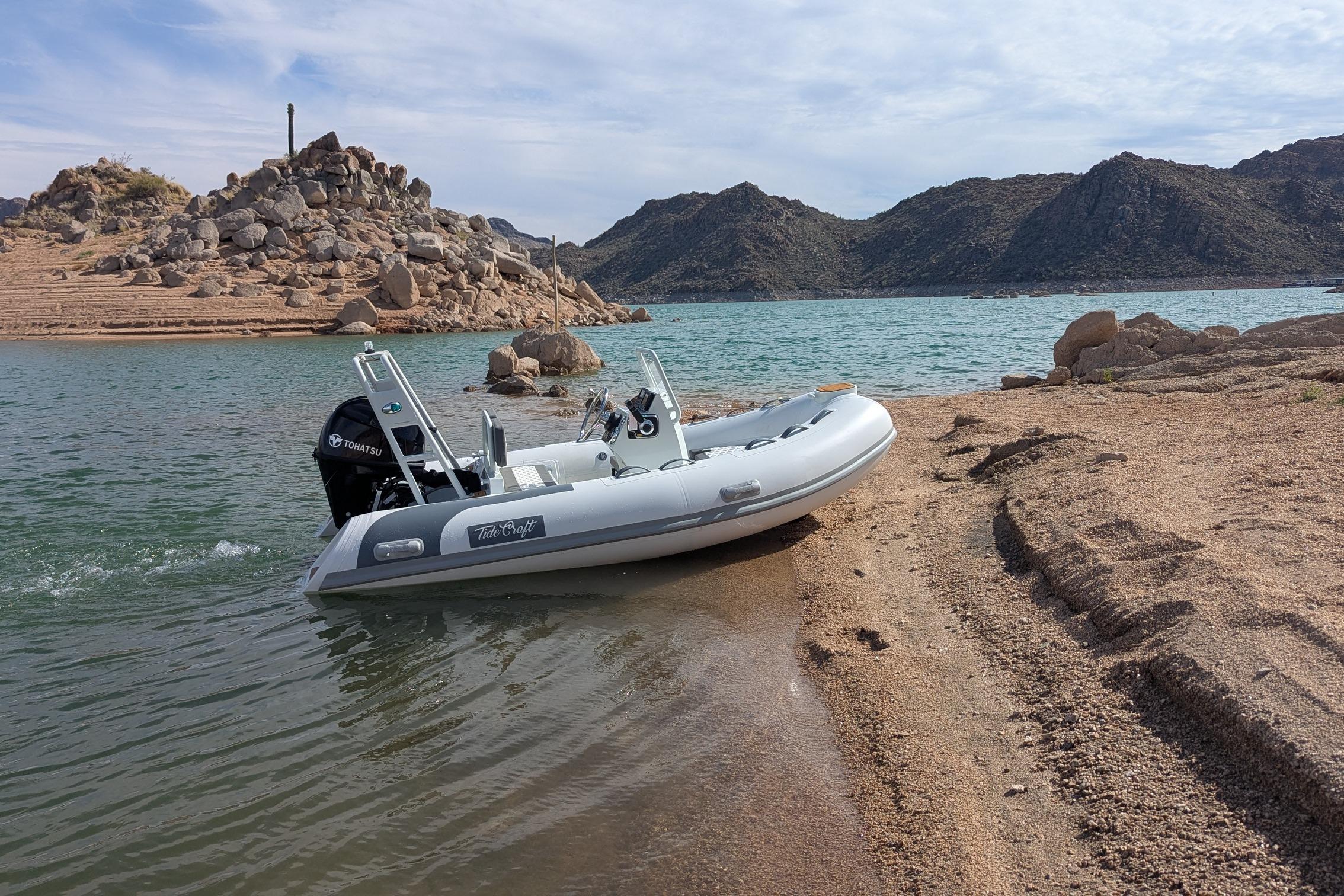 Tide Craft San Juan 11 boat on sandy shore, 2027 model, with rocky landscape background.