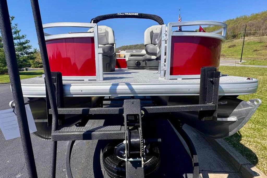 2026 Sun Tracker Bass Buggy 16 XL Select pontoon boat on trailer, red exterior, parked outdoors.